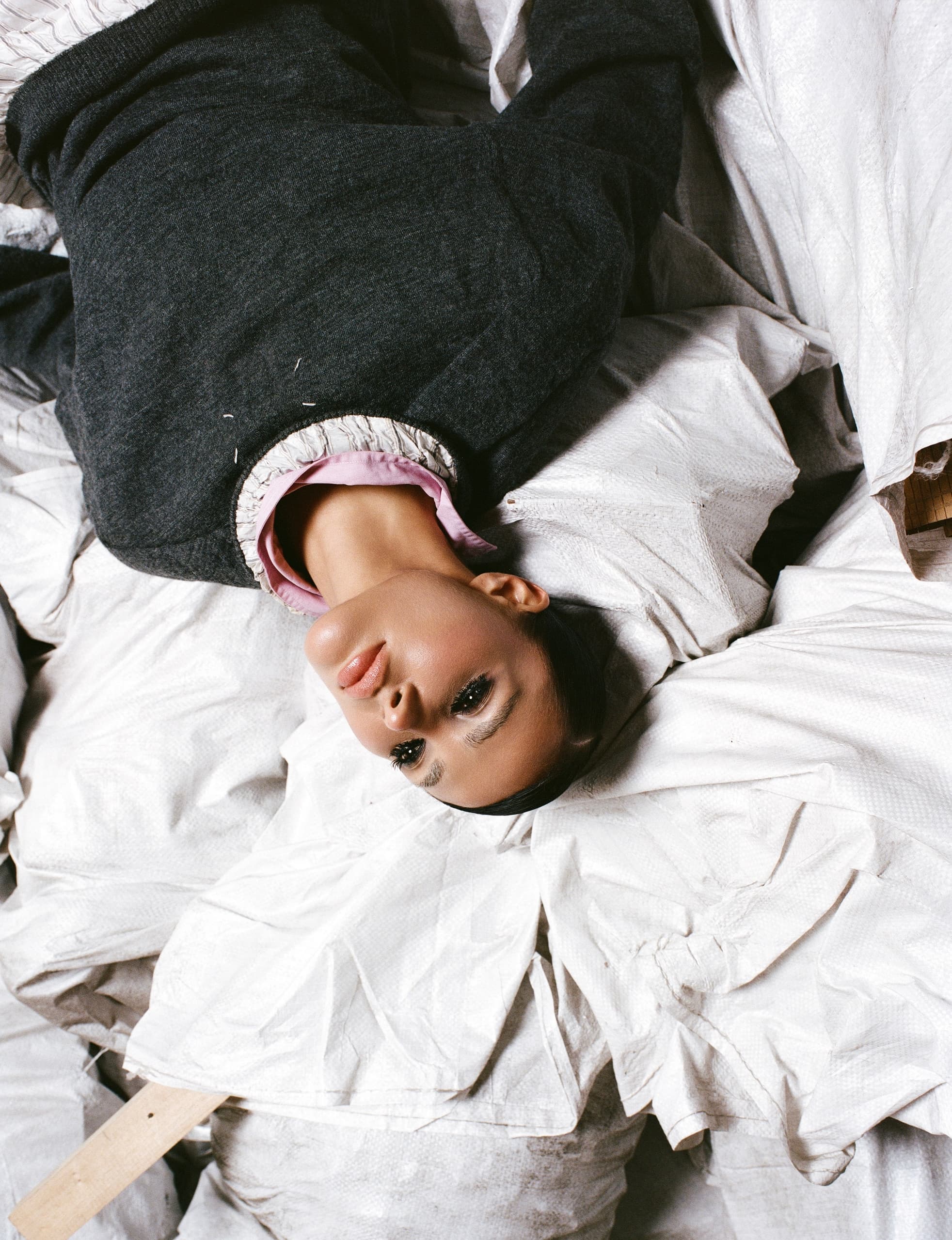 Upside-down woman in dark sweater lying on white textured bags.
