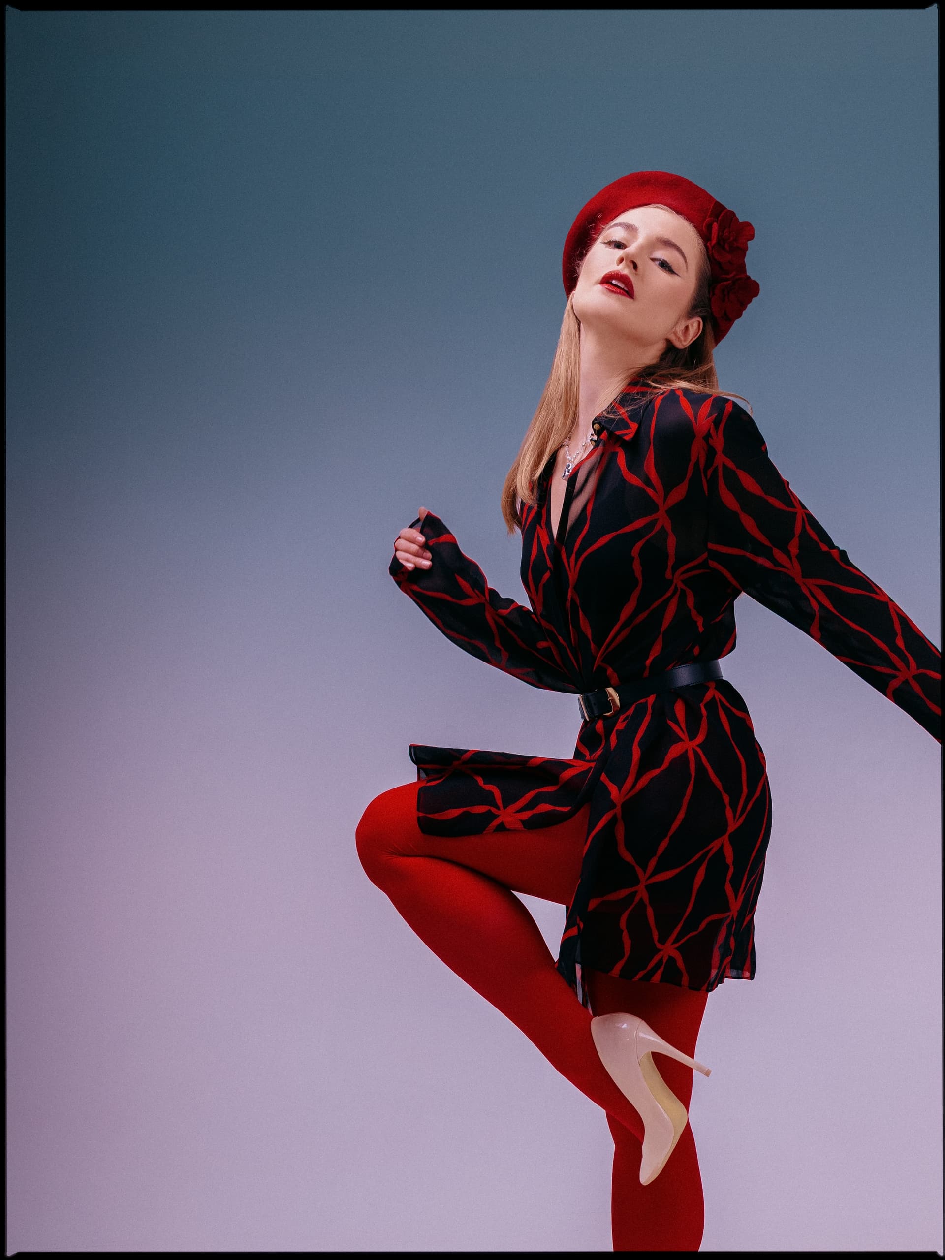 Elegant woman in red beret and patterned dress striking a pose against gradient backdrop.