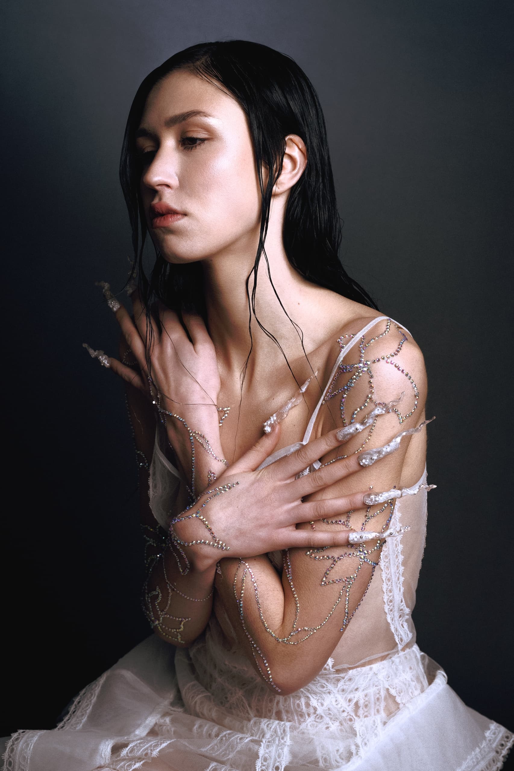 Artistic woman in jeweled dress, arms crossed, radiant and serene expression.