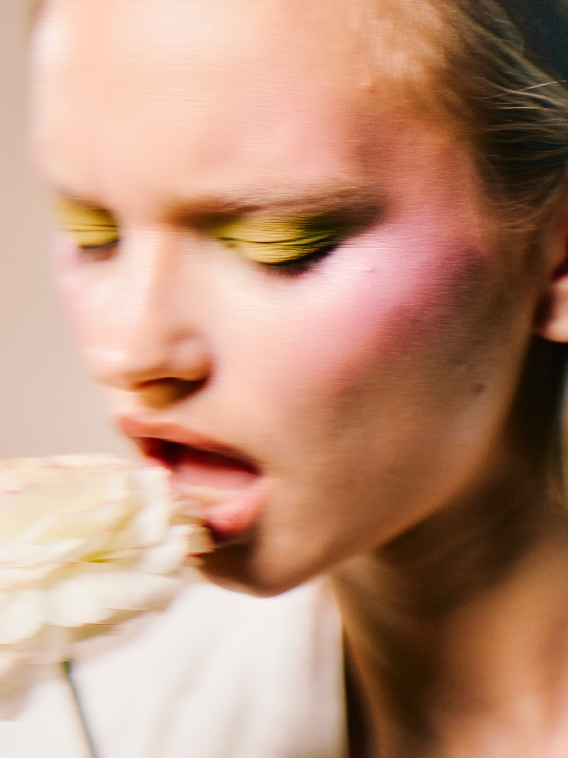 Woman with colorful makeup holding a flower artfully.