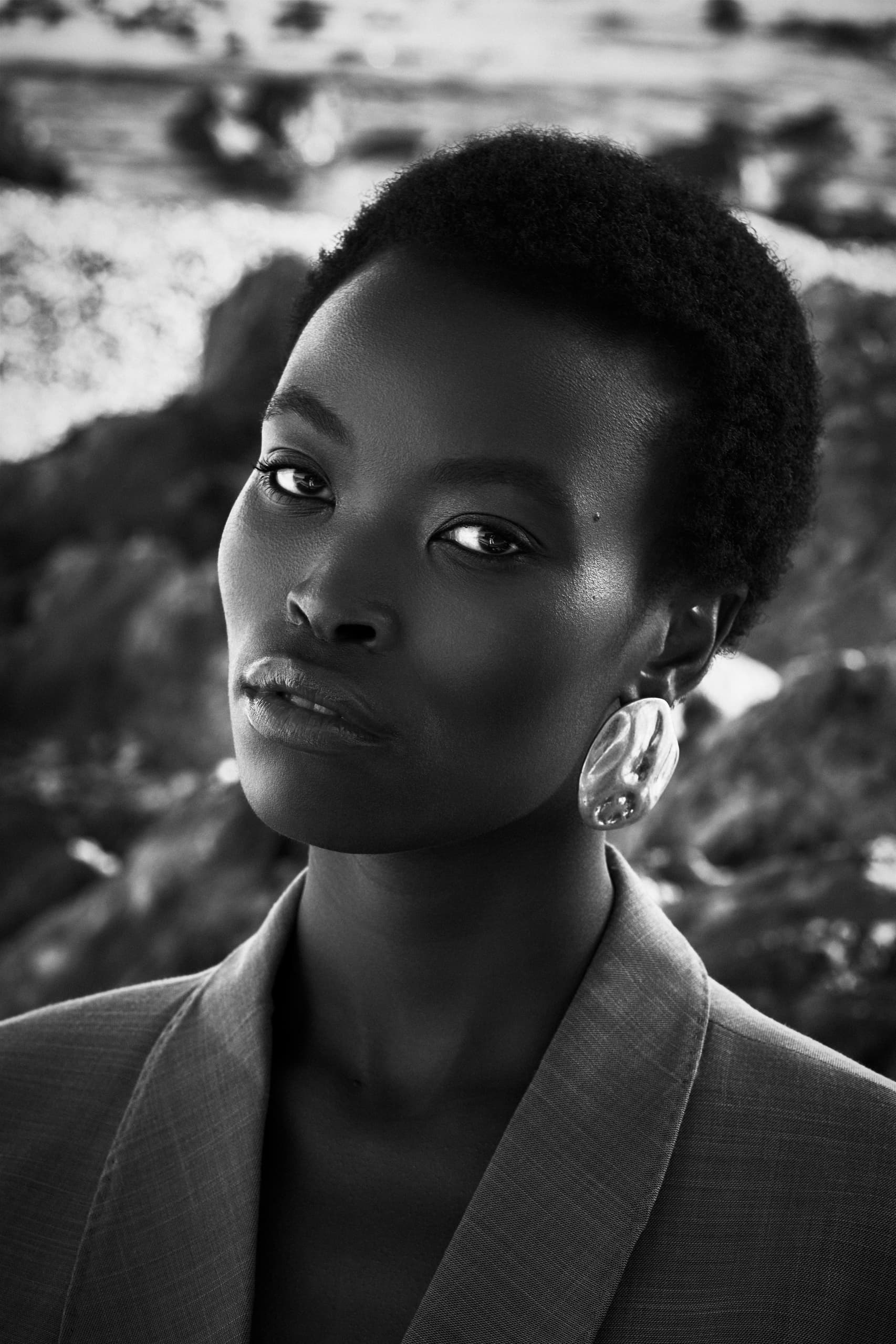 Stylish woman in blazer with bold earrings, black and white portrait photography.