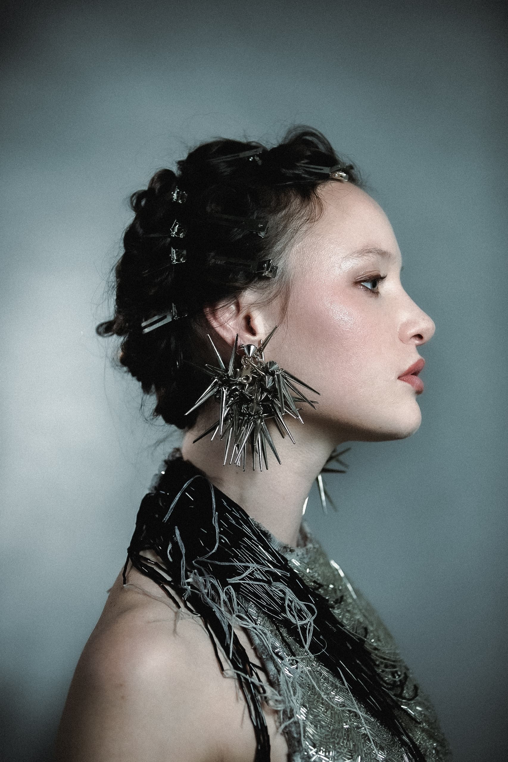 Stylish woman with spiky earrings and intricate updo against gray background.