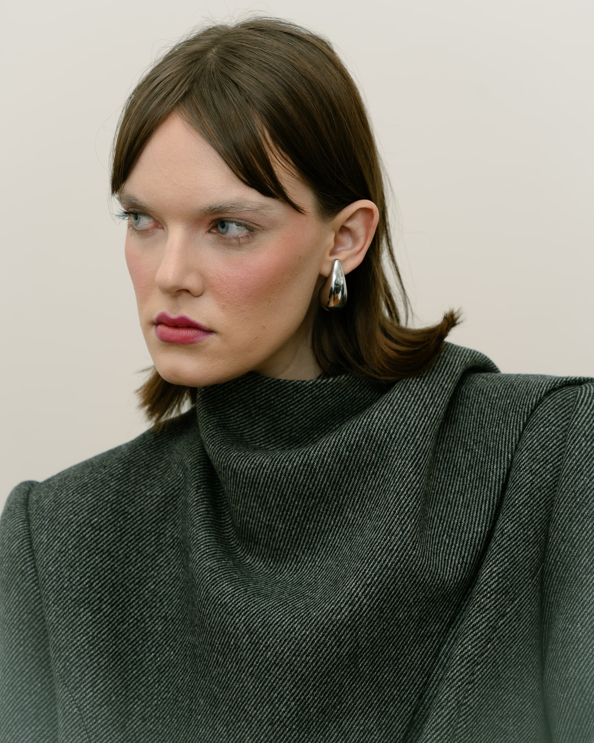 Woman in stylish gray top with statement earrings, gazing to the side.