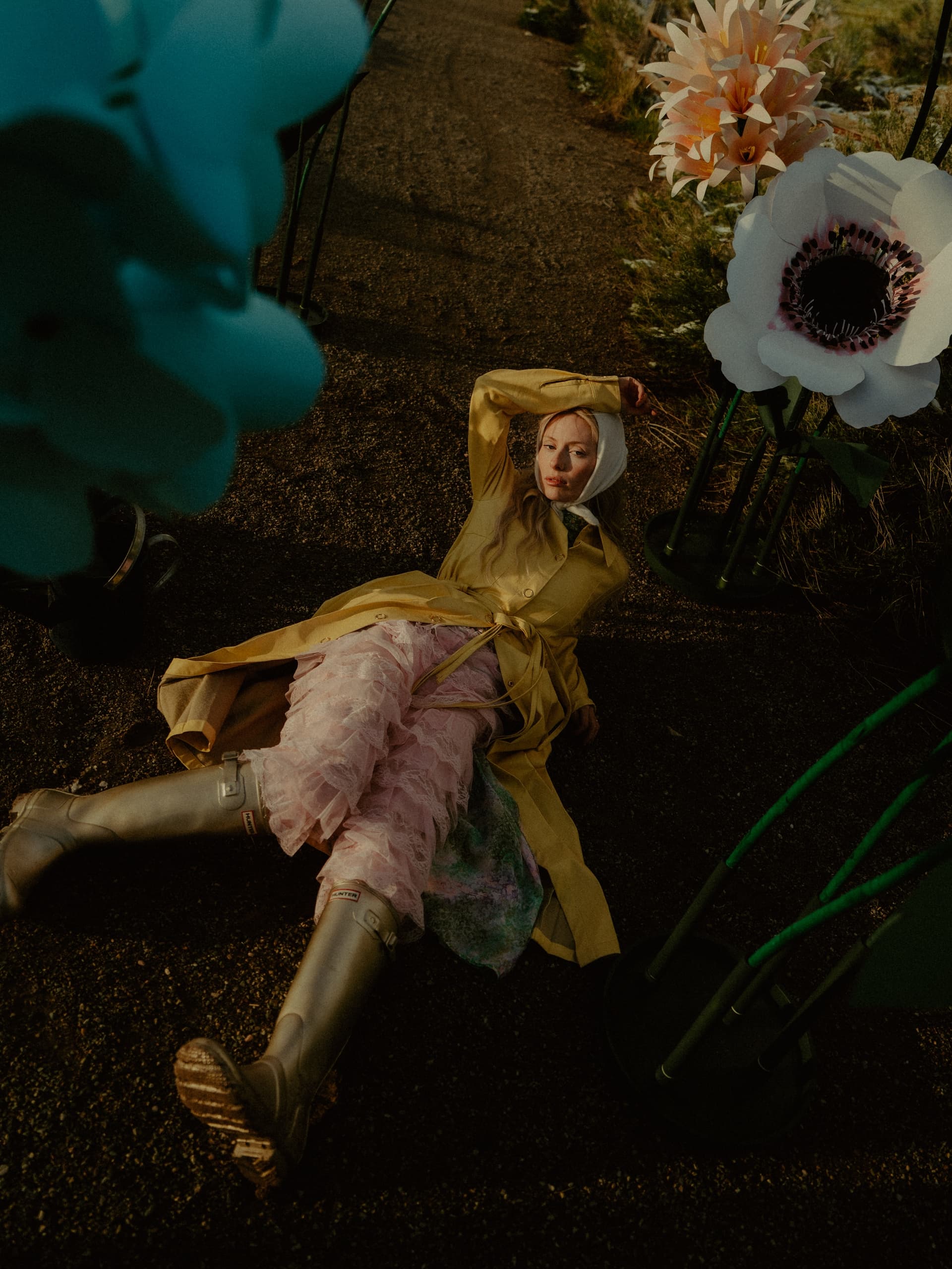 Person in fashion outfit relaxing beside large flowers on a garden path.