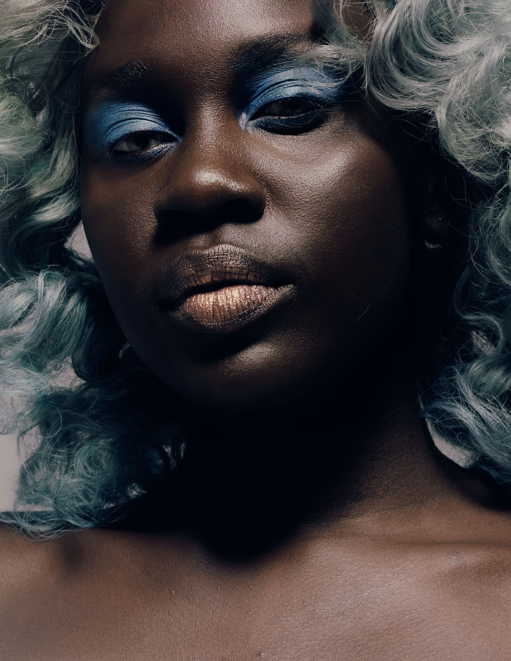 Close-up of a person with blue makeup and curly hair.