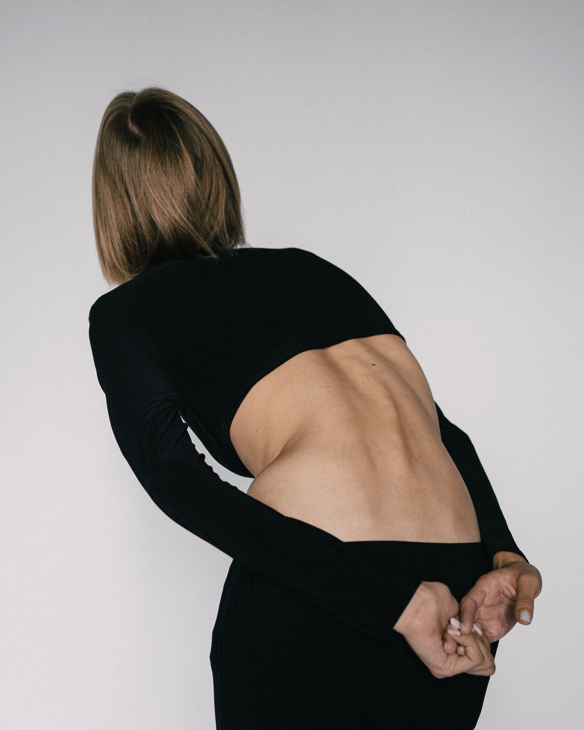 Person in black outfit, back exposed, bent over and hands clasped.