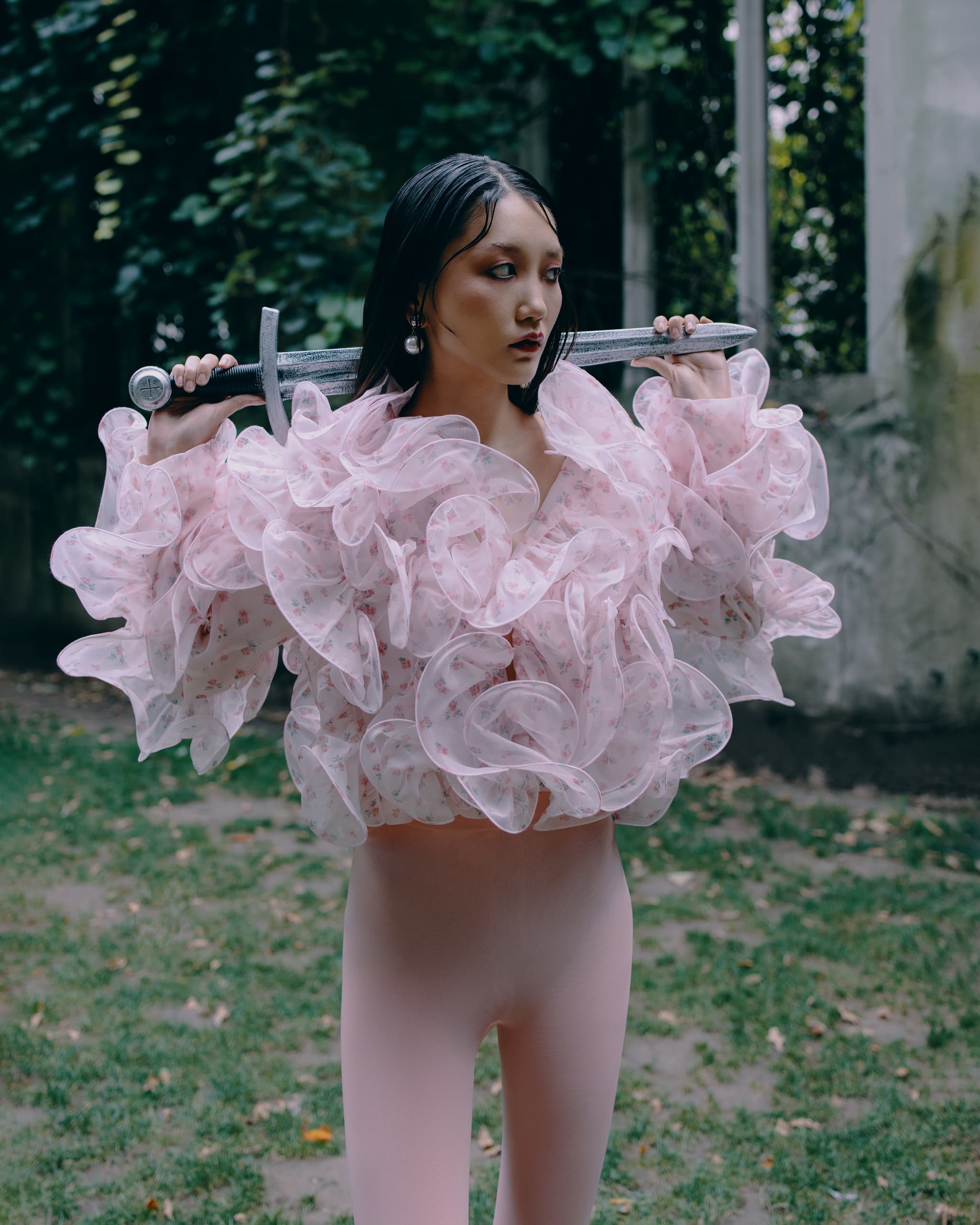 Woman in floral blouse holding sword in garden setting. Fashion and strength theme.