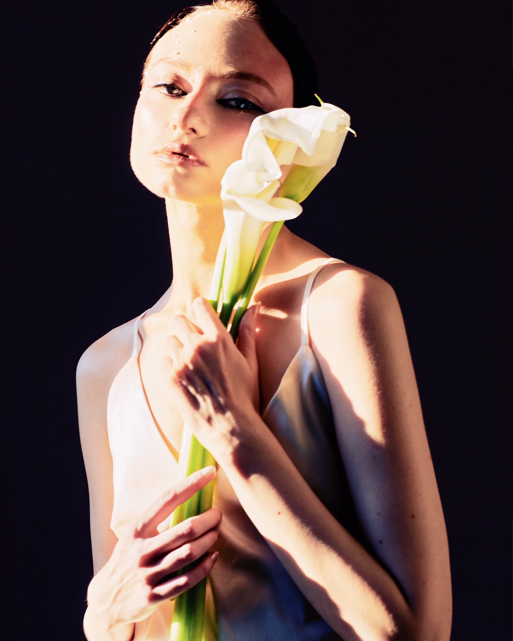 Model in elegant dress holding white calla lilies in dramatic lighting.