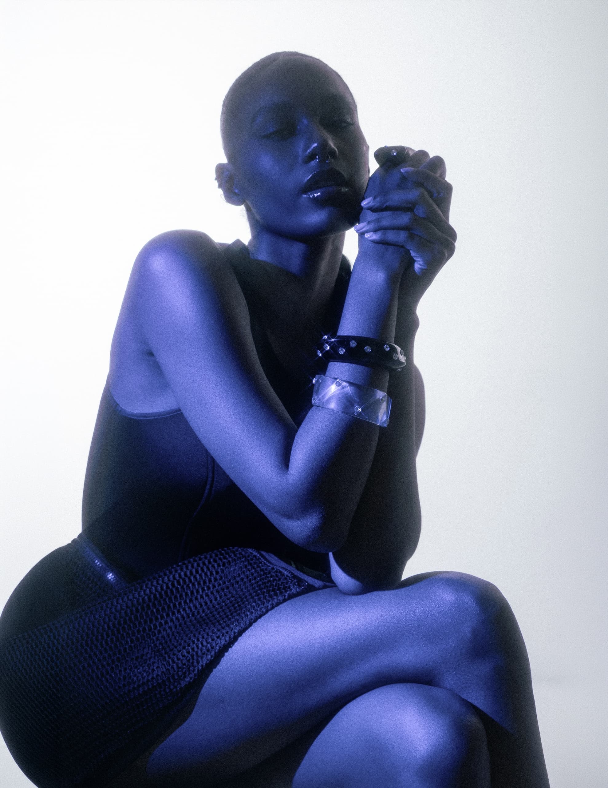 Fashion model in striking blue light, wearing bracelets and elegant outfit.