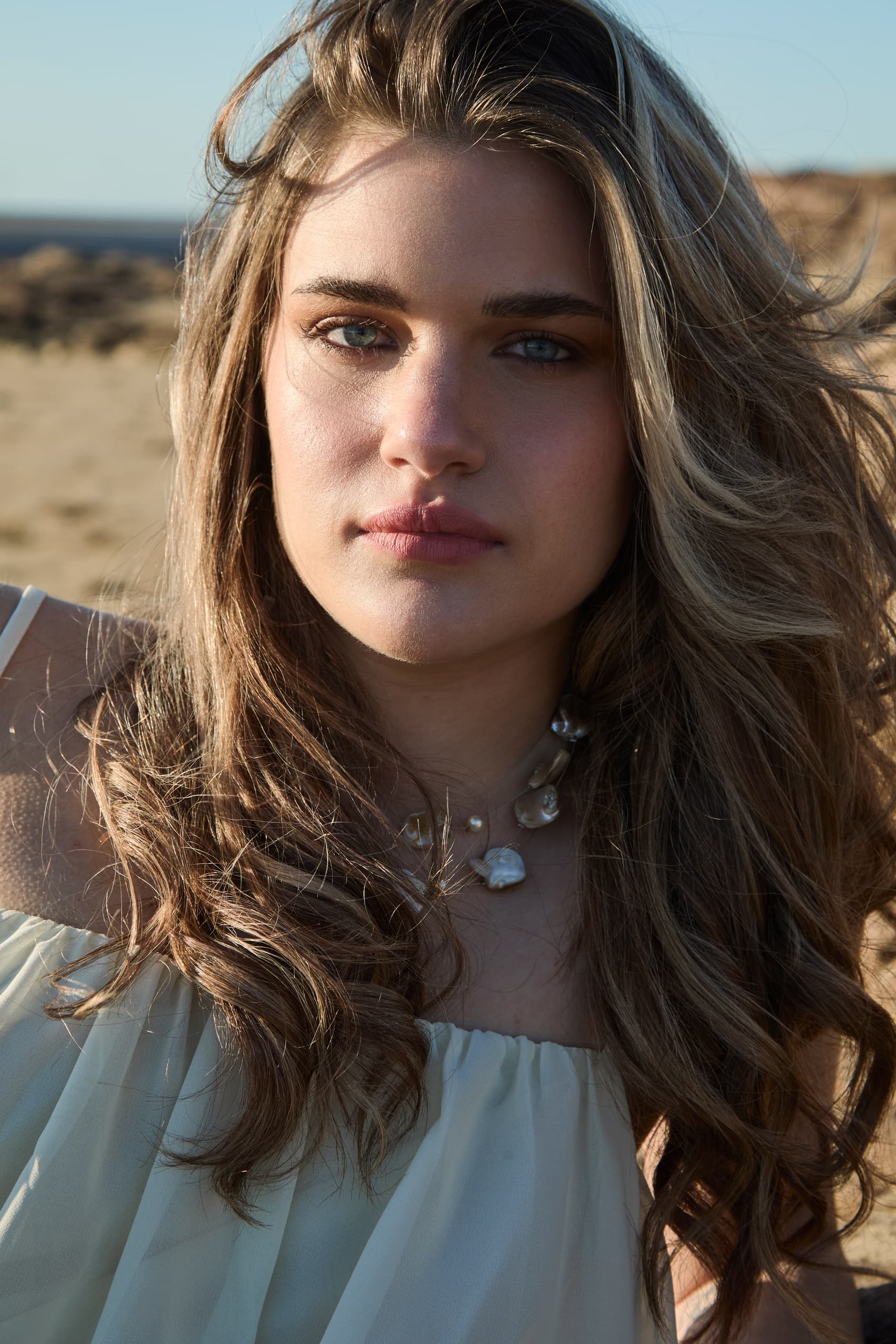 Woman with wavy hair and necklace at the beach.