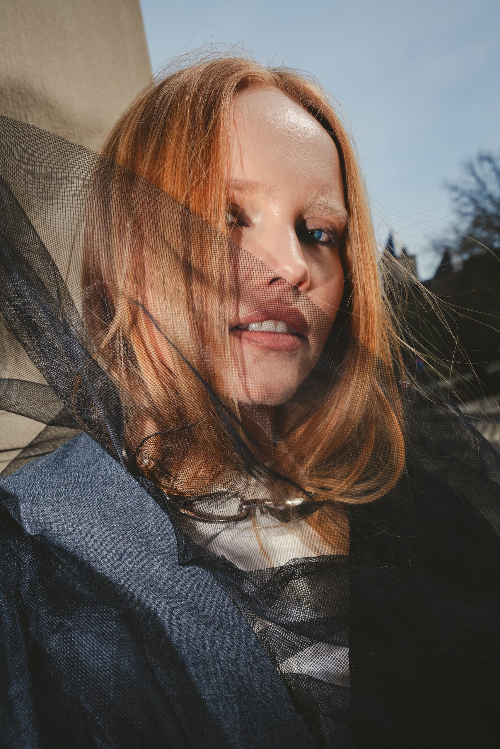 Stylish woman with red hair and tulle outdoors on a bright day.