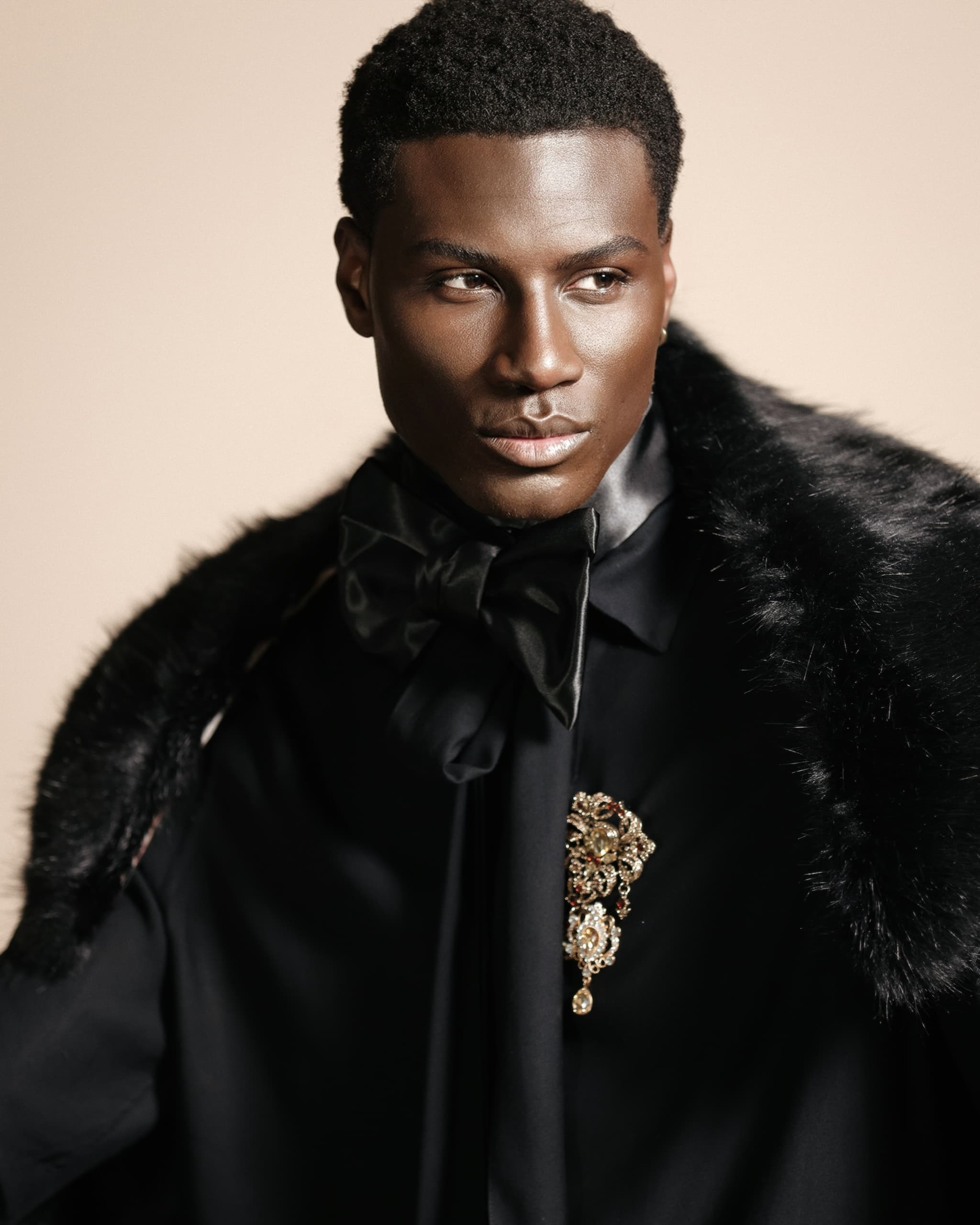 Stylish man in elegant black outfit with fur and ornate brooch.