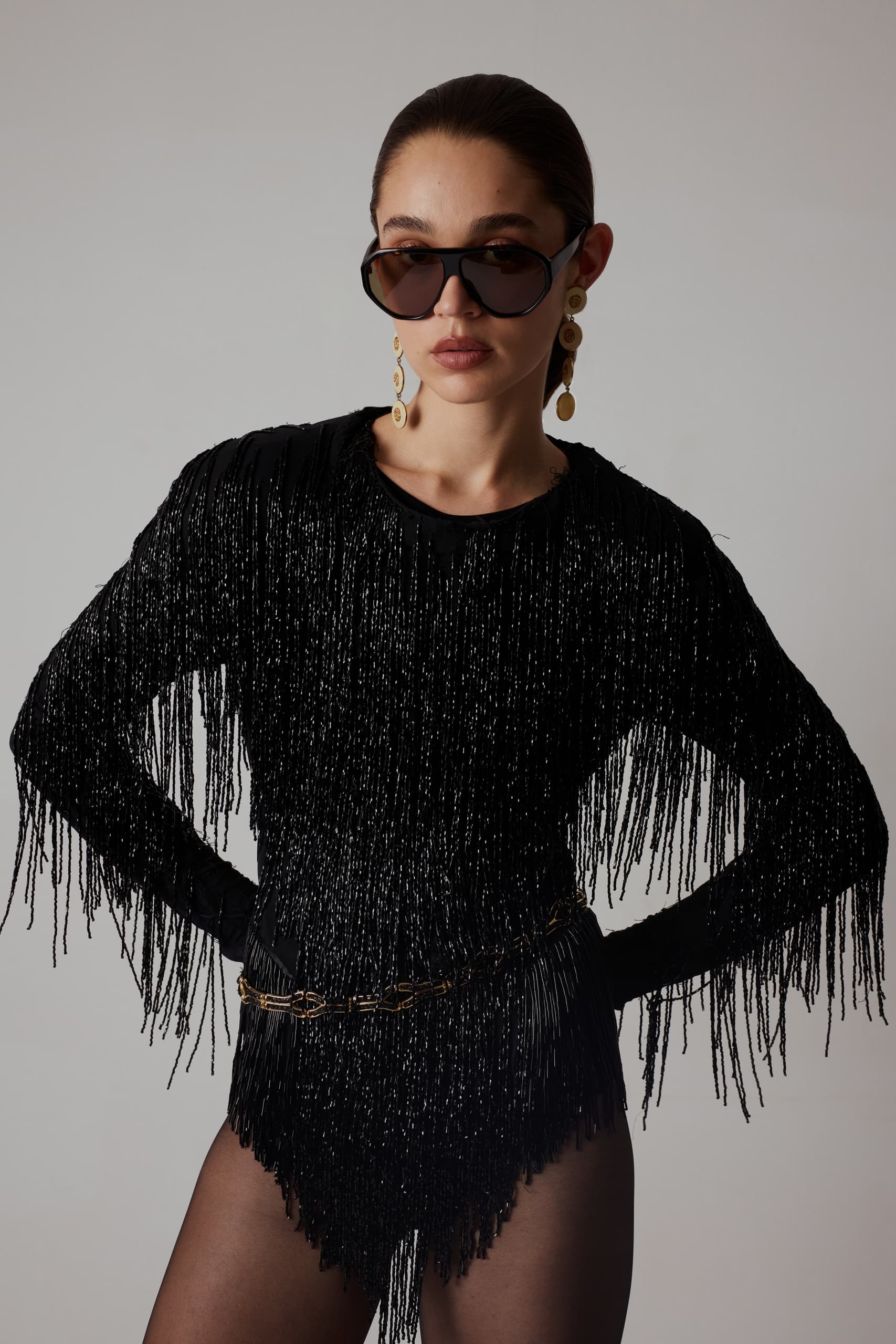 Stylish woman in black fringe outfit with sunglasses and bold earrings.