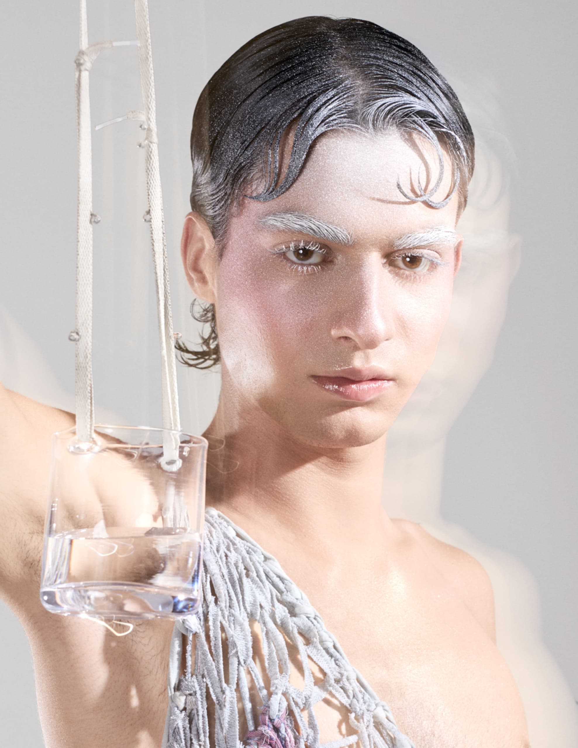 Futuristic fashion portrait with artistic makeup and net dress holding a glass of water.