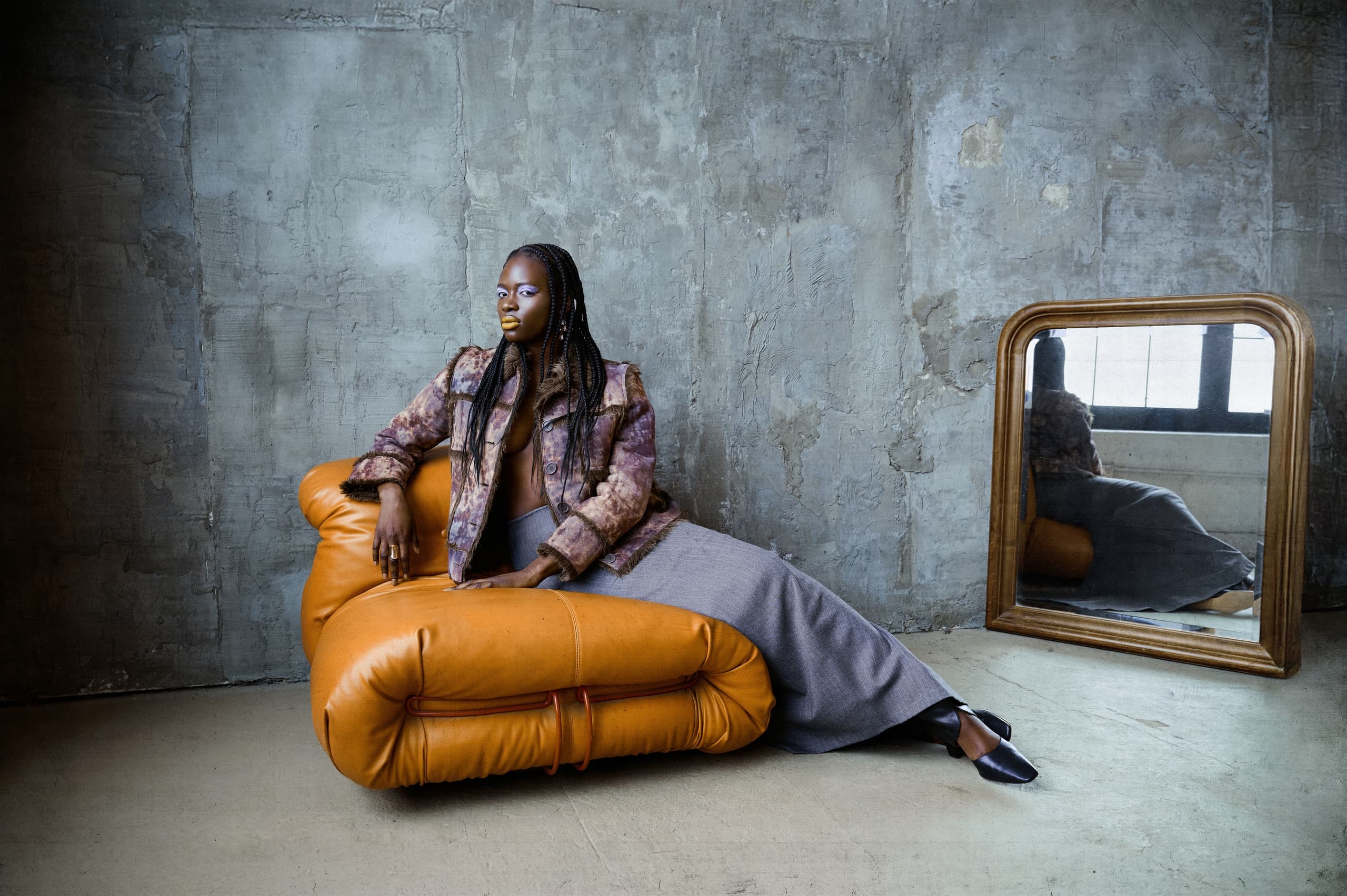 Stylish woman lounges on tan leather chair in industrial-chic setting.