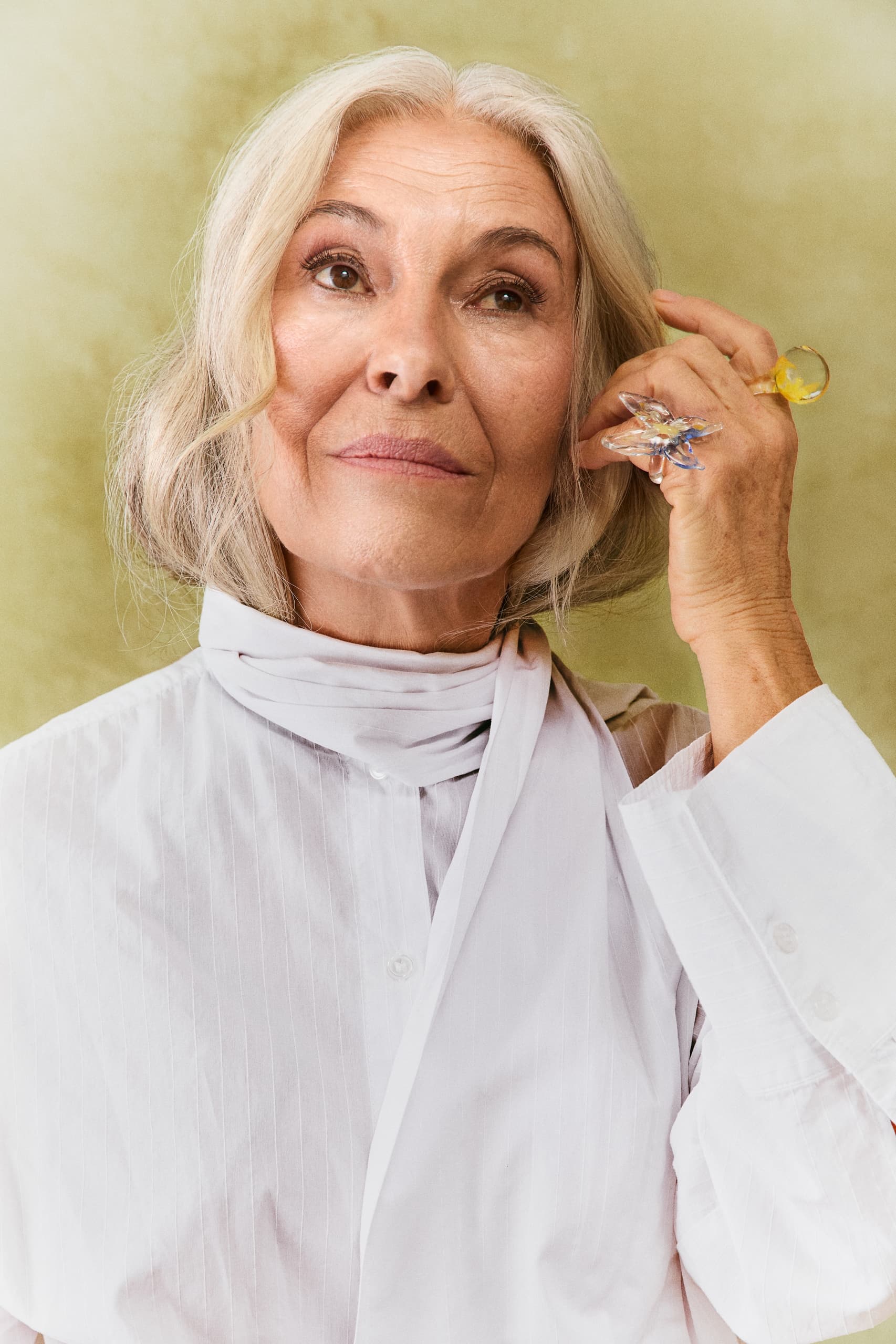Elegant woman in white shirt with stylish ring, green background.