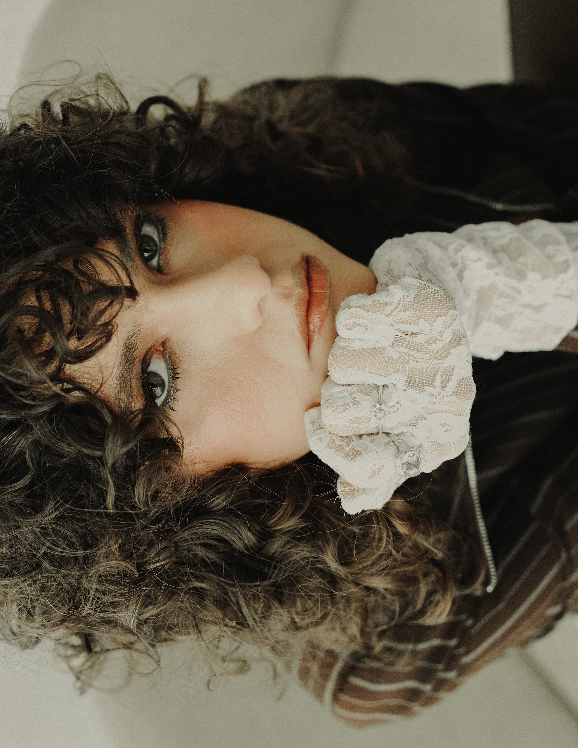 Woman with curly hair wearing lace glove, gazing thoughtfully.