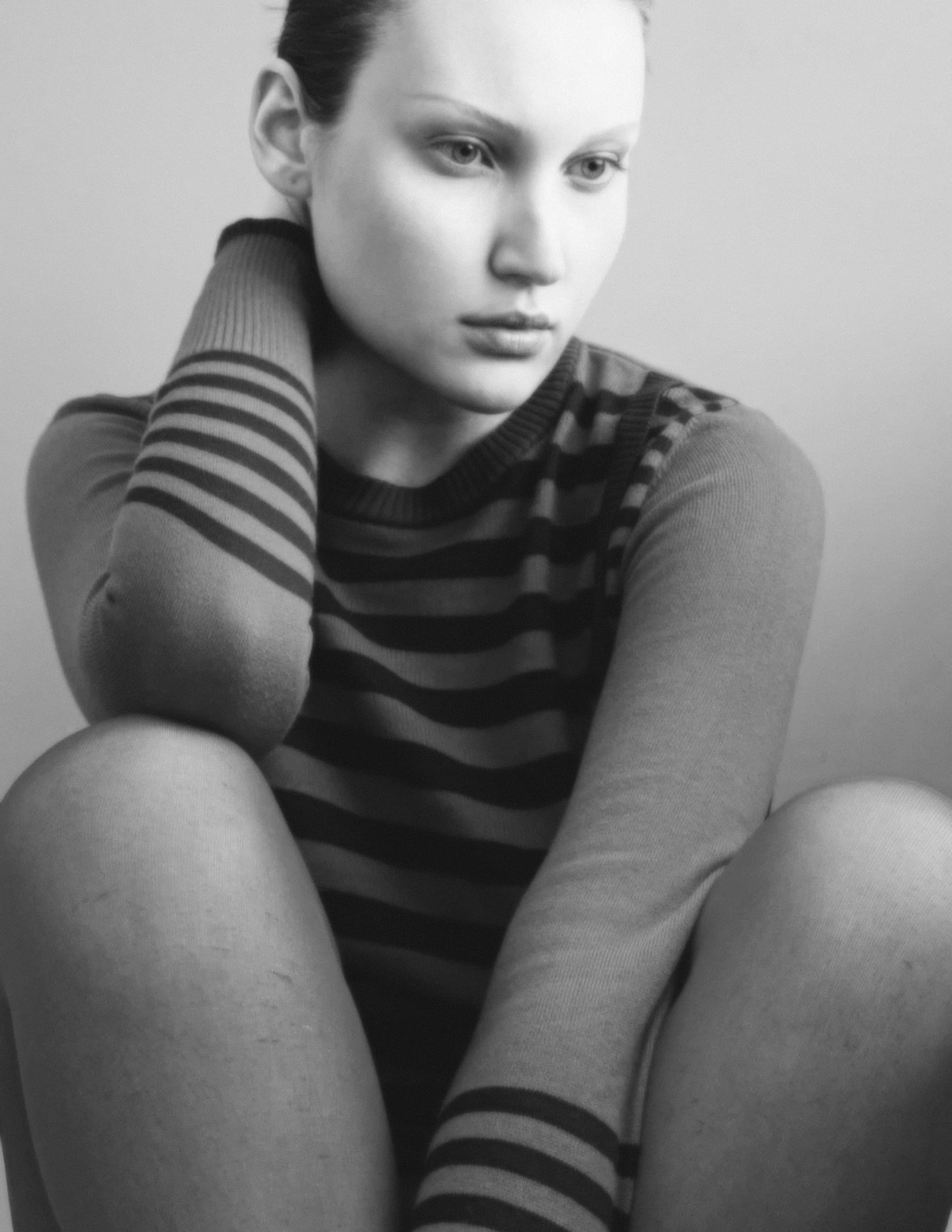 Black and white portrait of a thoughtful person sitting, wearing a striped sweater.
