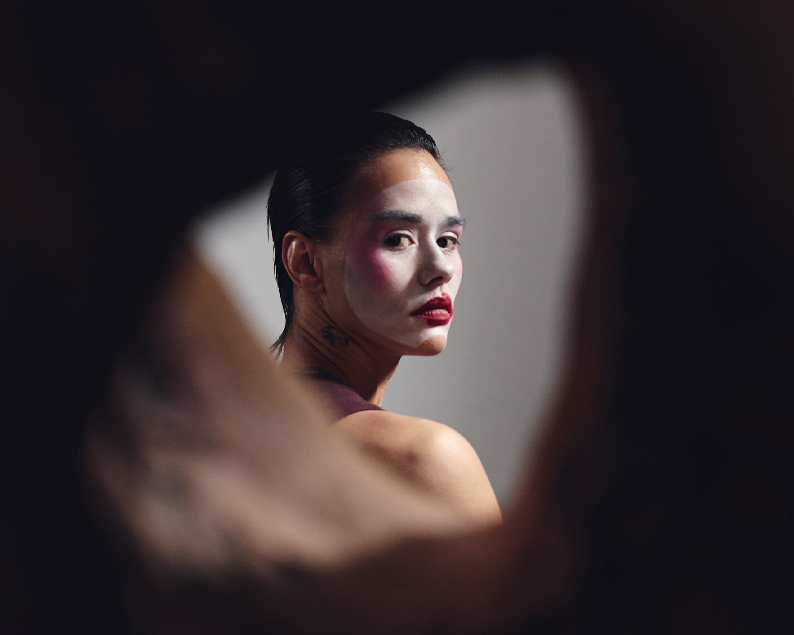 Person with artistic makeup glancing through abstract frame, dramatic lighting enhances look.