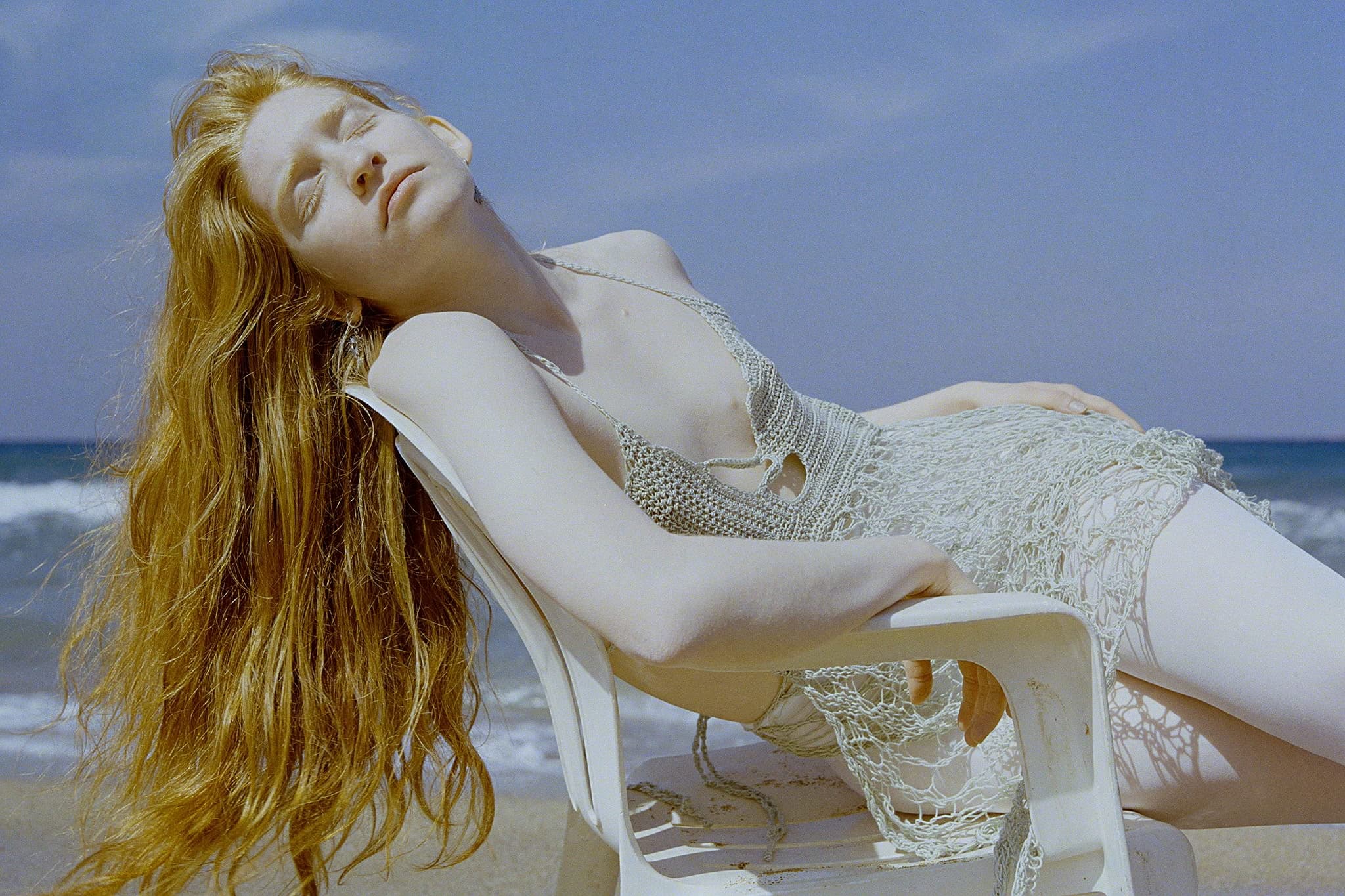 Person relaxing in a beach chair with long hair, enjoying sunlight by the ocean.