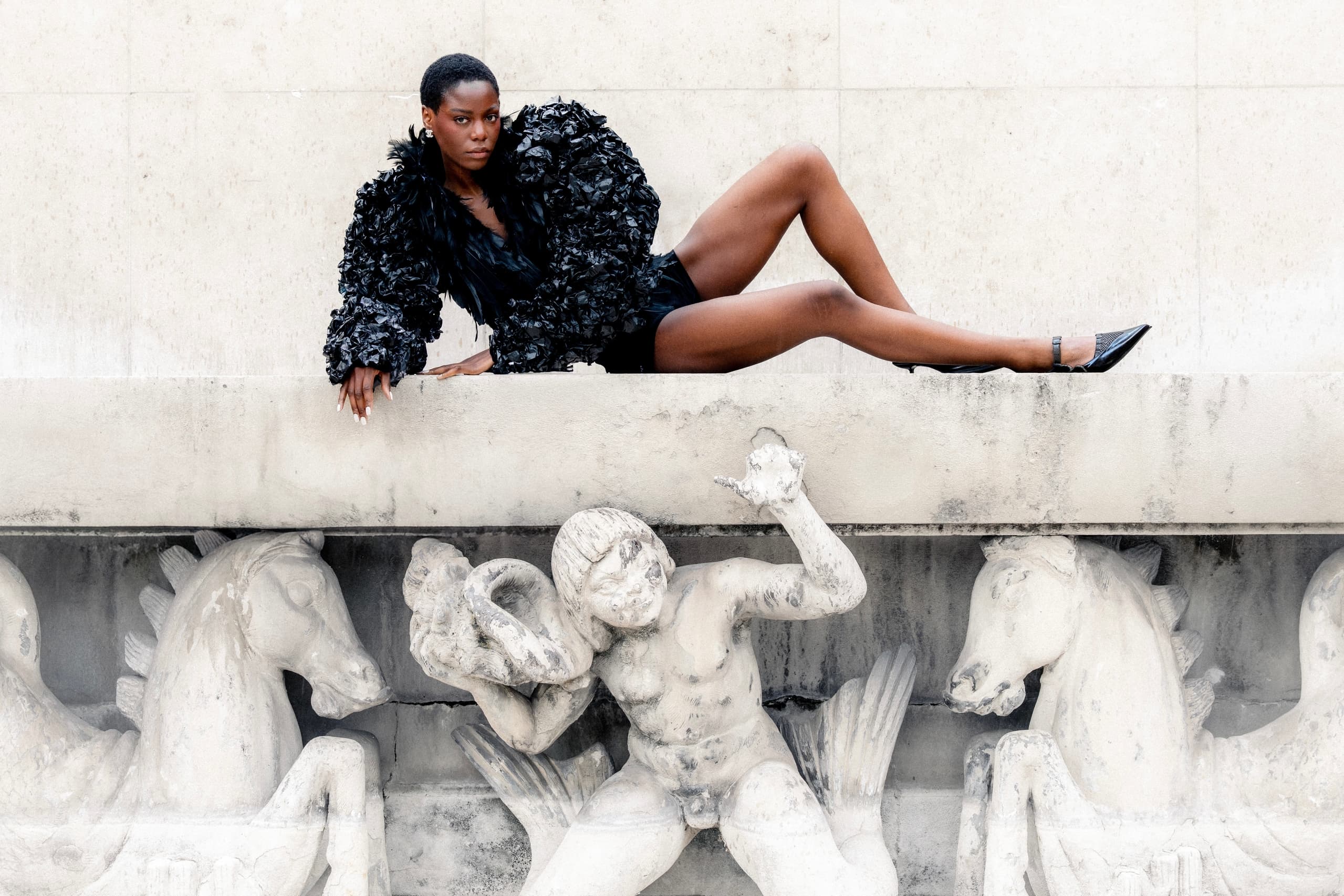 Model in bold black outfit poses on ornate stone sculpture.