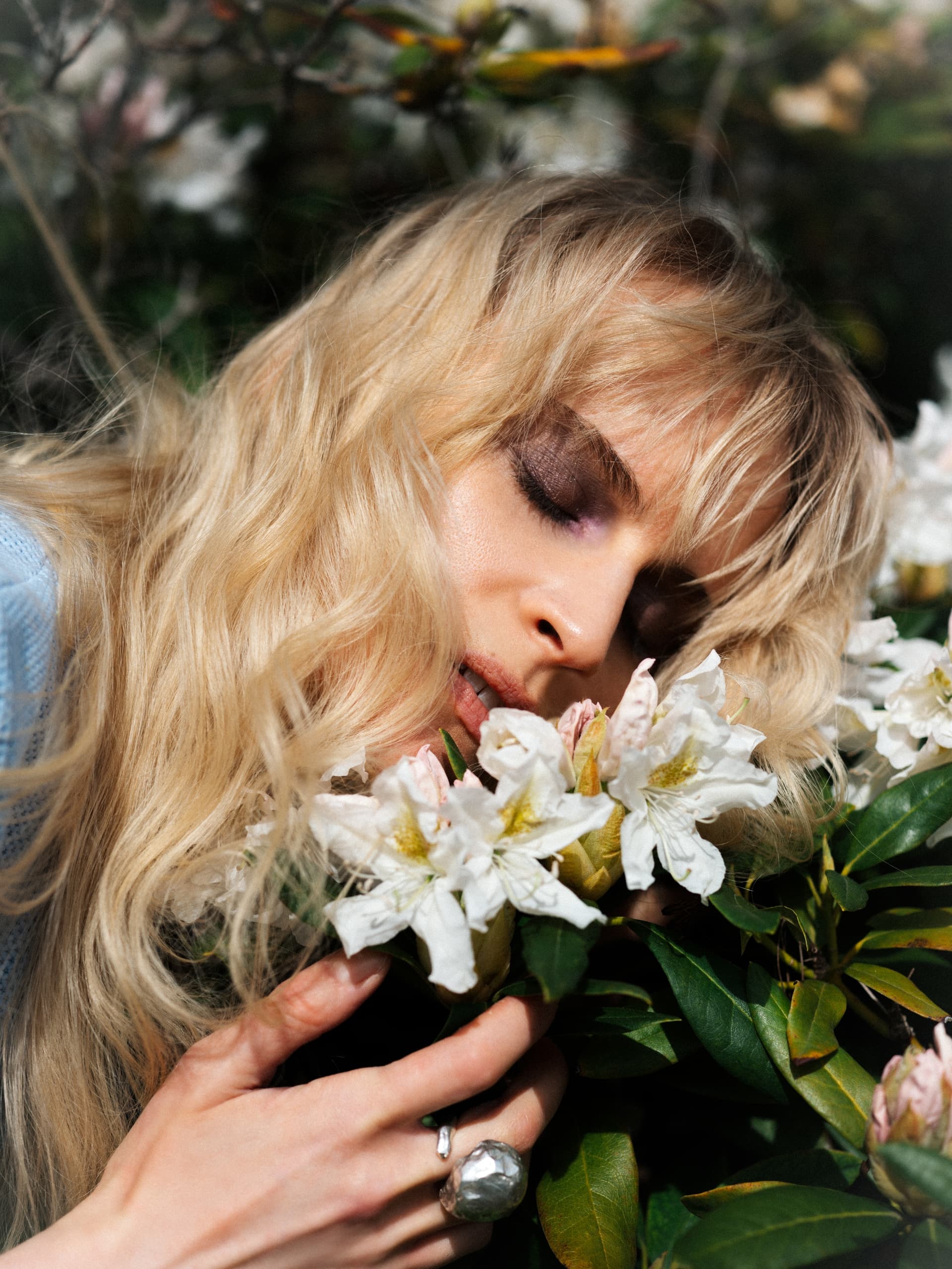 Woman enjoying the scent of white flowers in a lush garden.
