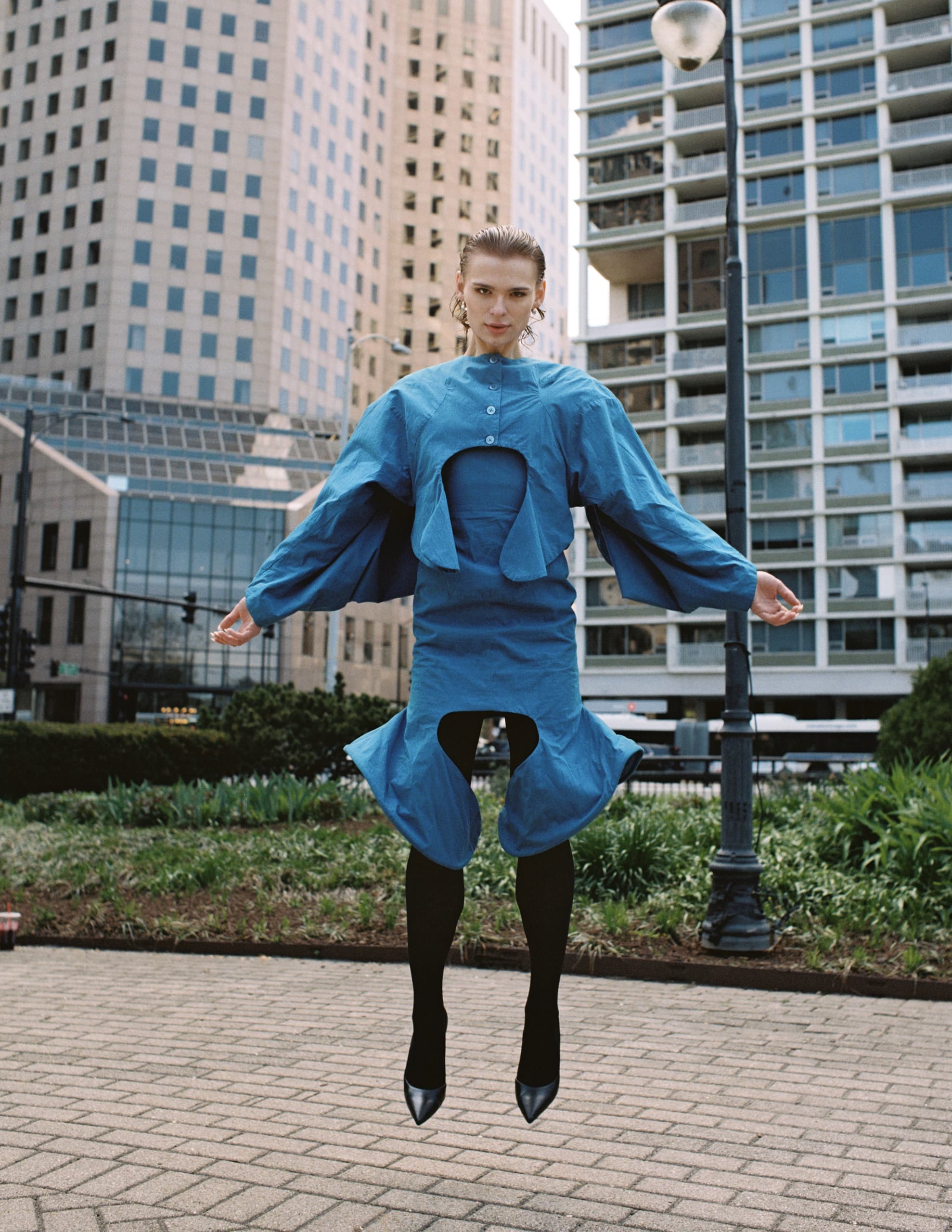Woman in blue dress jumping with city buildings in the background.