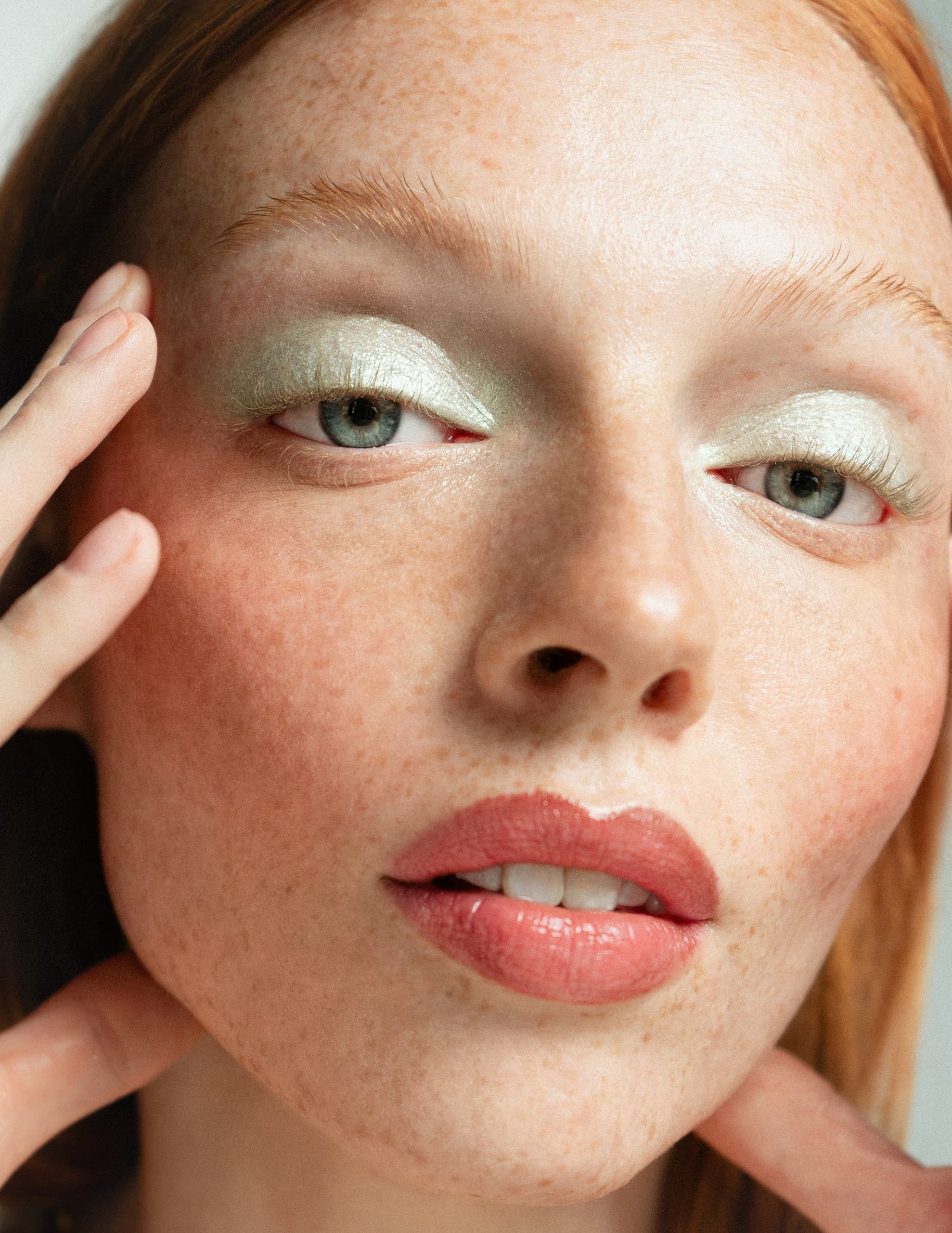 Woman with shimmering green eyeshadow and natural freckles, close-up beauty shot.