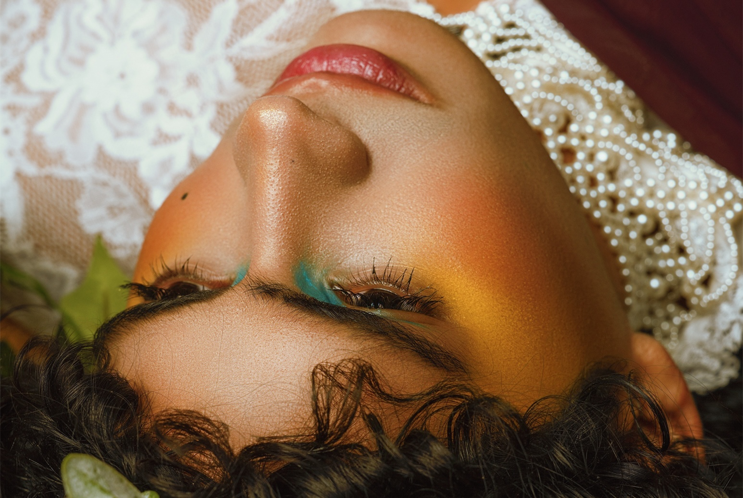 Person in artistic makeup lying down, wearing lace and pearls.