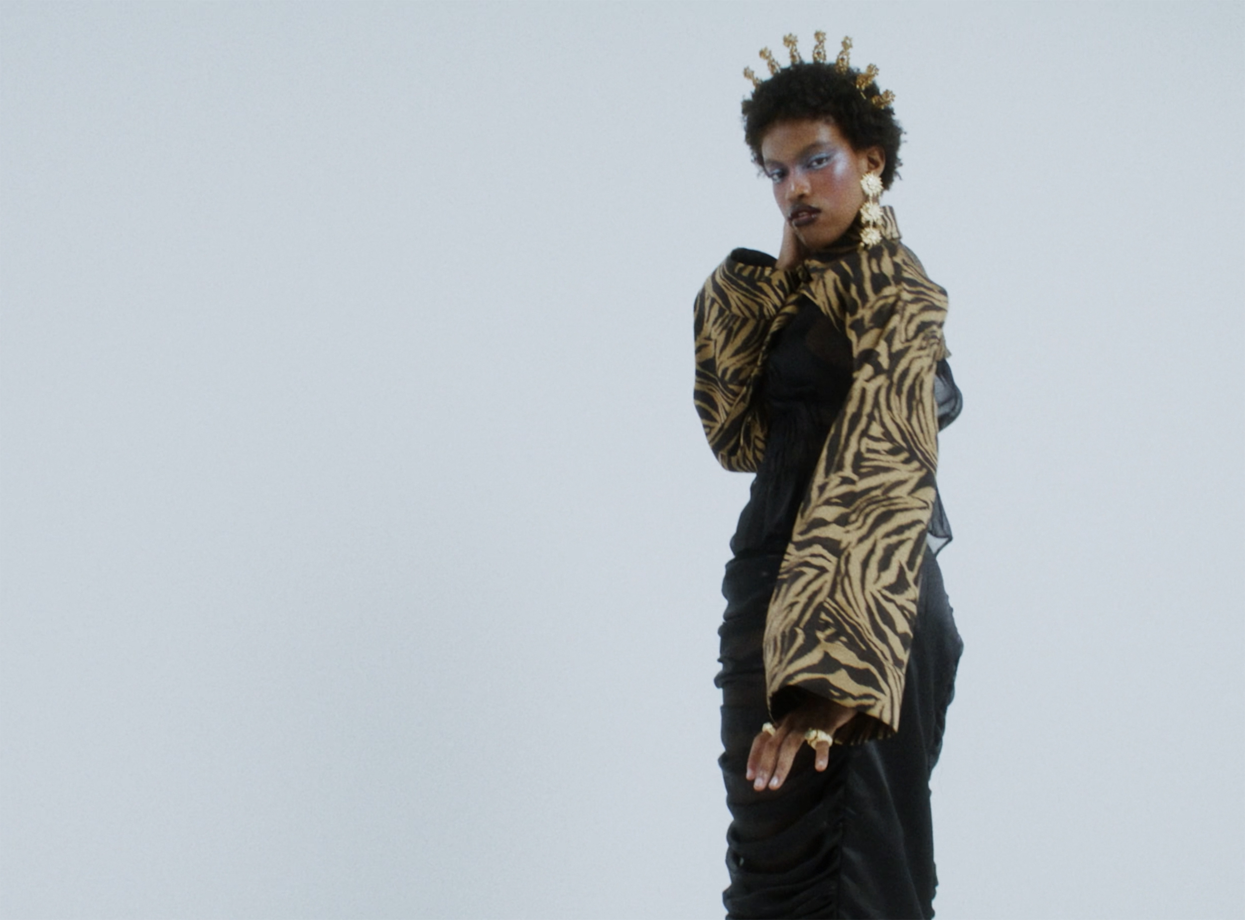 Person in a striking outfit with headpiece, zebra-patterned sleeves, and bold makeup.