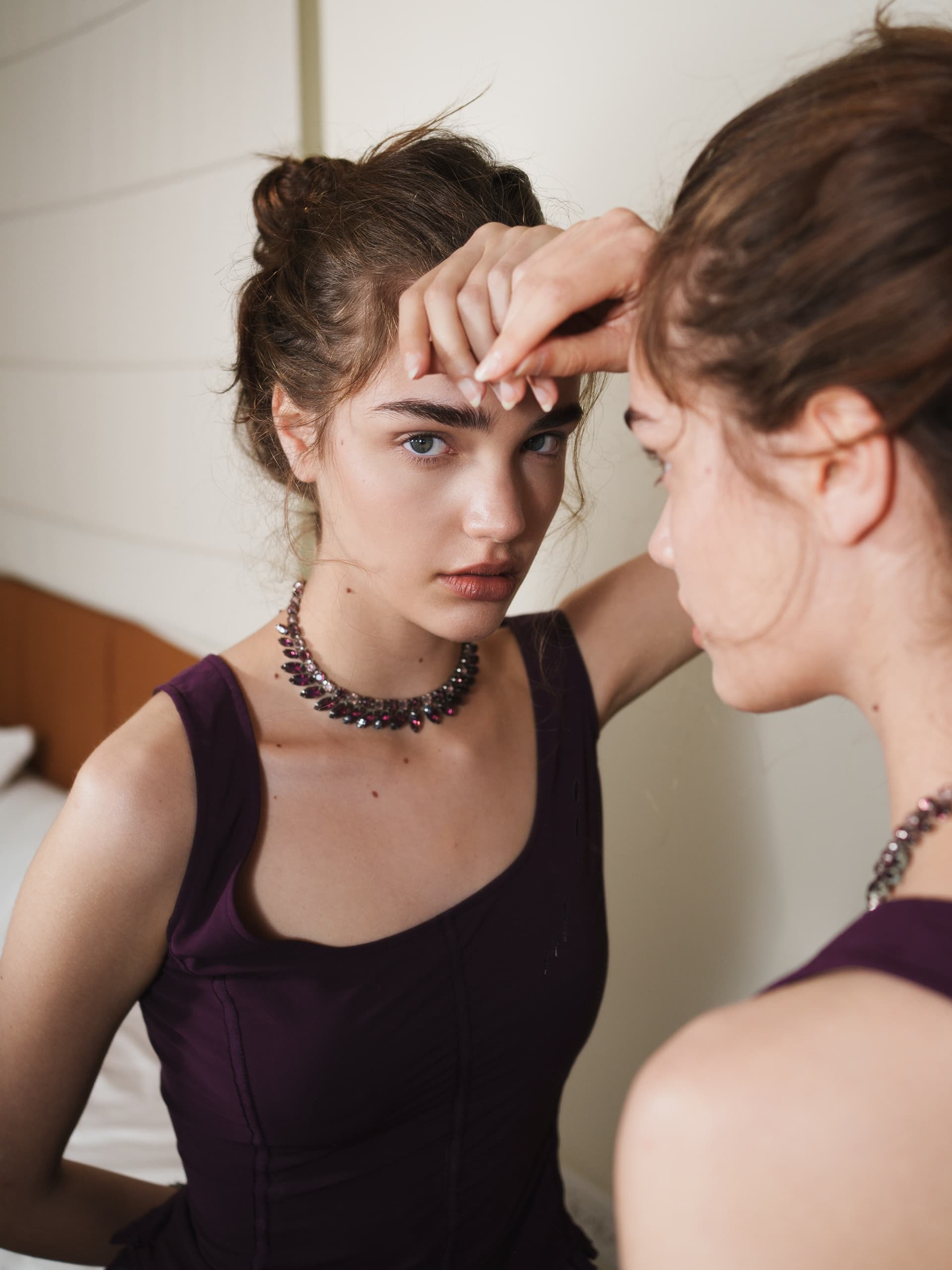 Woman gazing into mirror wearing elegant necklace and dark dress.