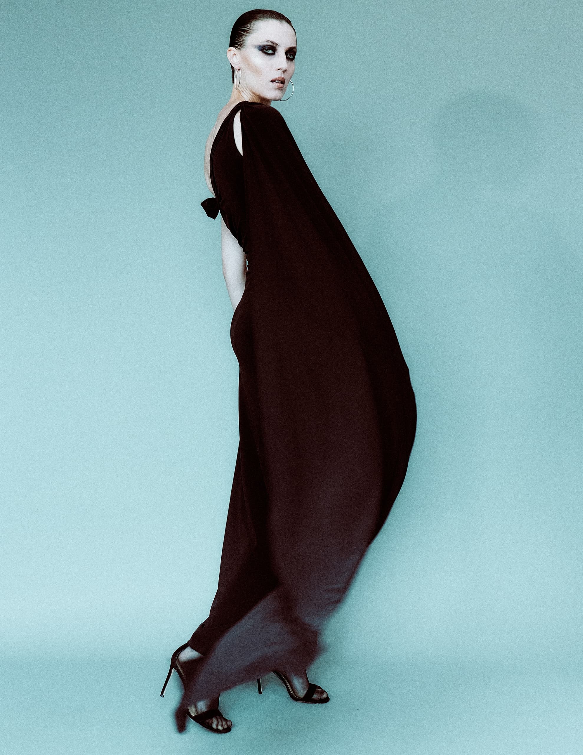 Elegant woman in flowing black gown with striking makeup and high heels.