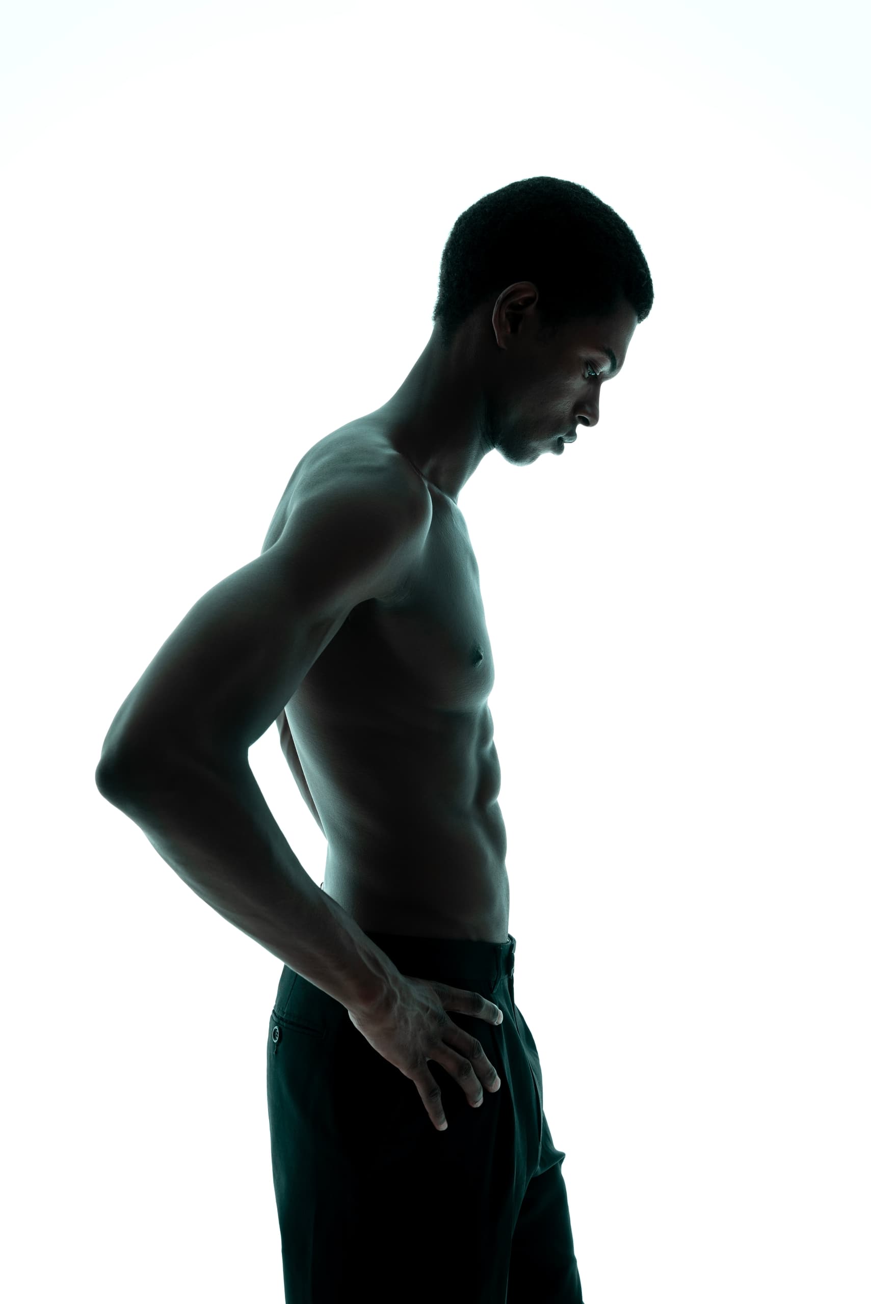 Silhouette of a shirtless man in profile, hands on hips, against a white background.