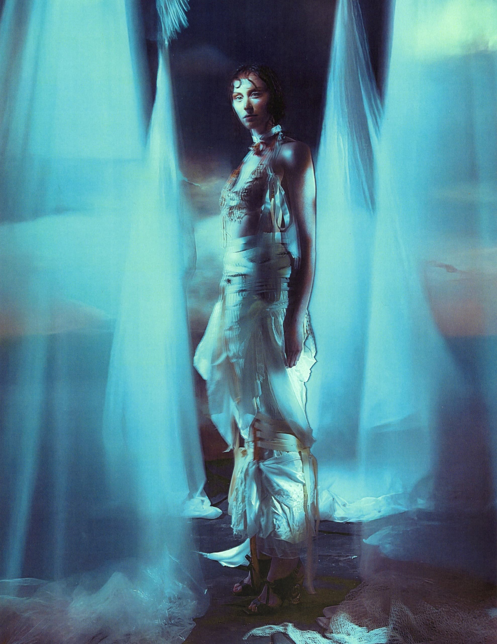 Mysterious woman in flowing gown surrounded by ethereal, sheer blue fabric.