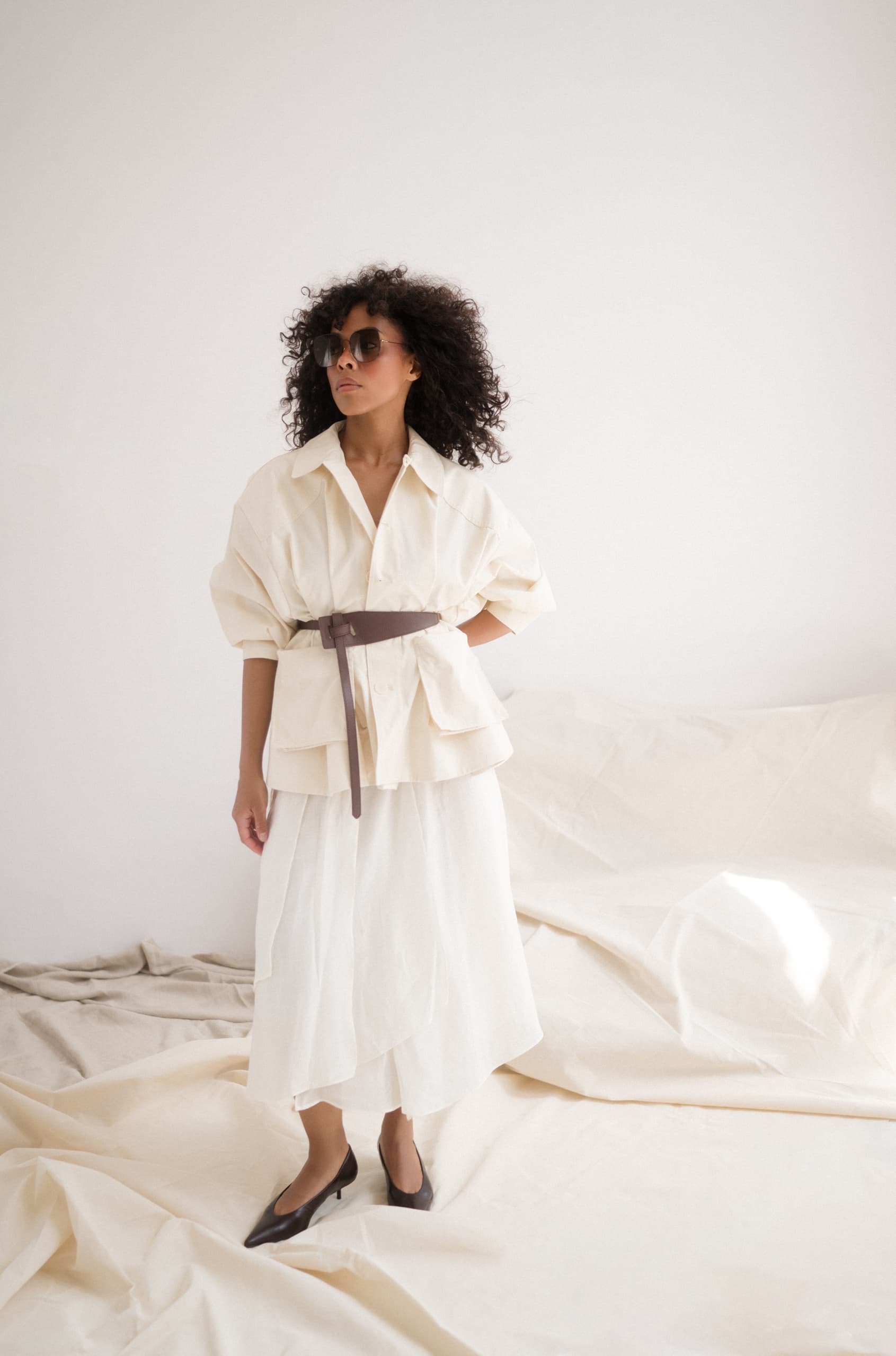 Fashionable woman in cream outfit and sunglasses in minimalist setting.