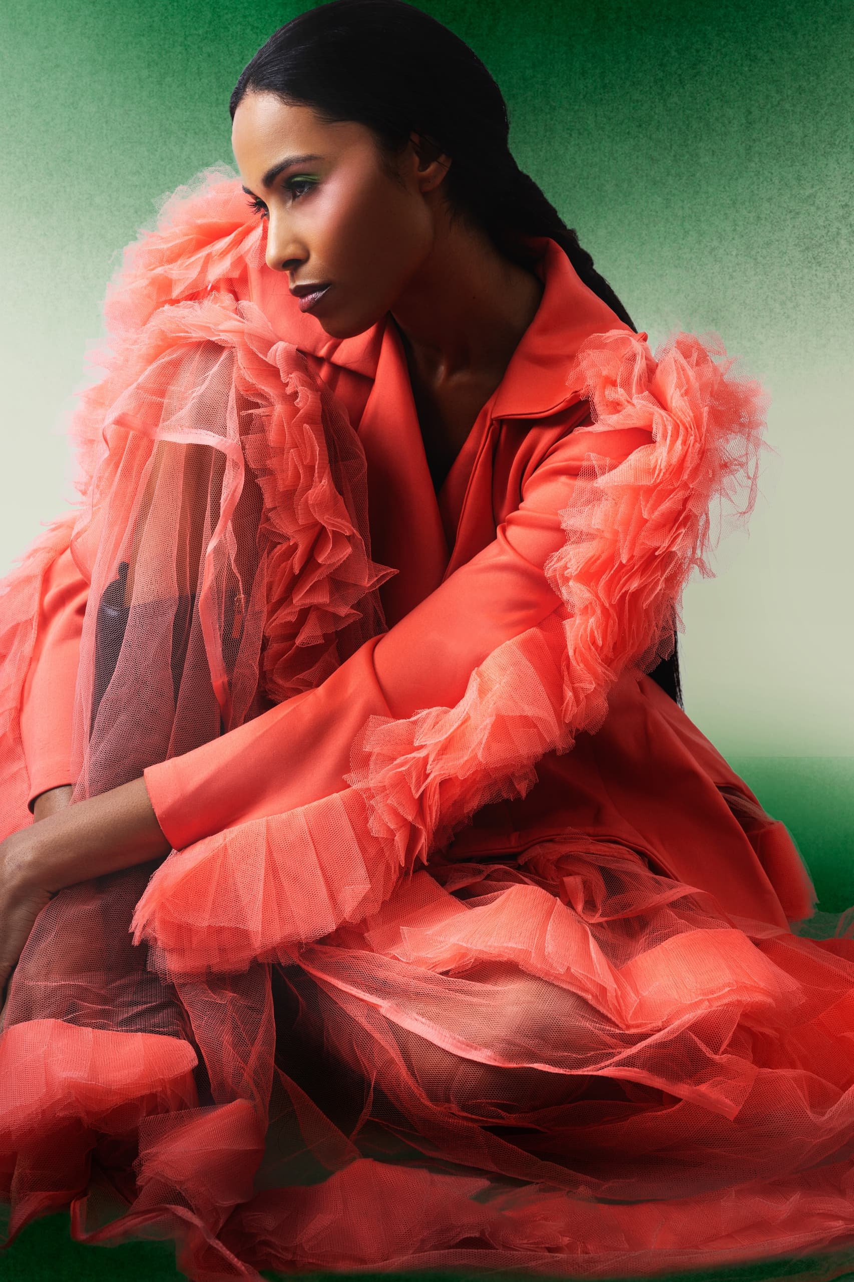 Woman in coral tulle fashion outfit sitting against a green background.