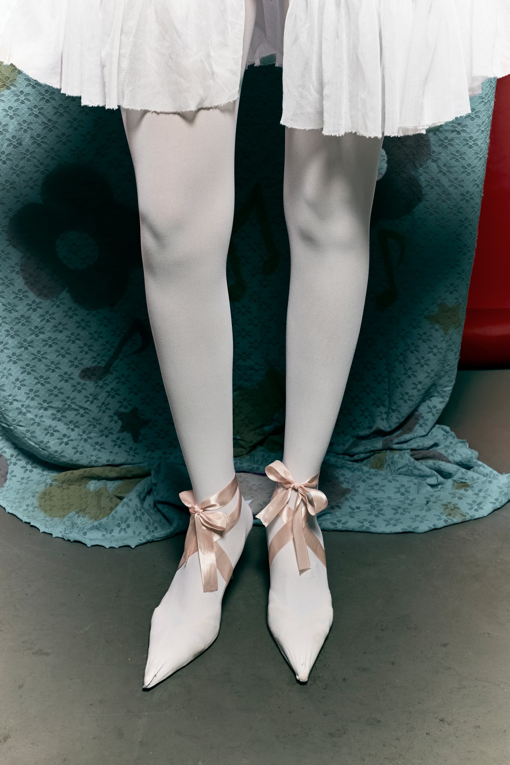 Ballet dancer's legs in white tights and pointe shoes with ribbon bows.