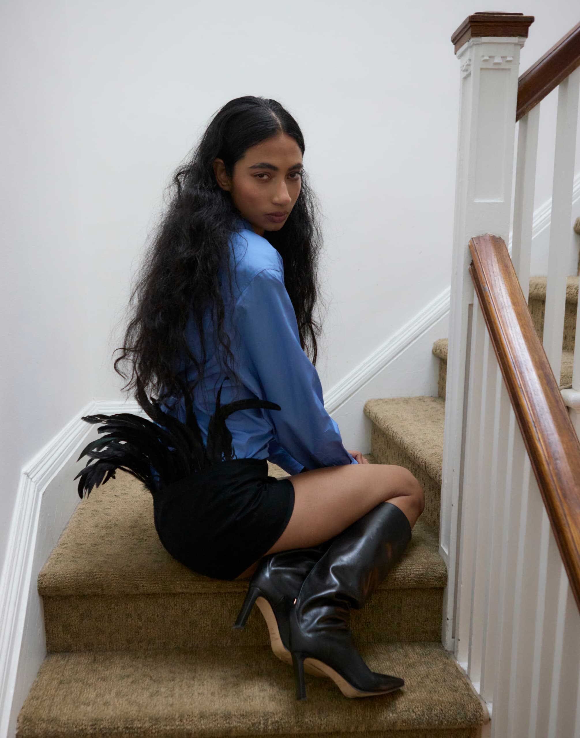 Person in a blue shirt sitting on stairs wearing black boots and feathered shorts.