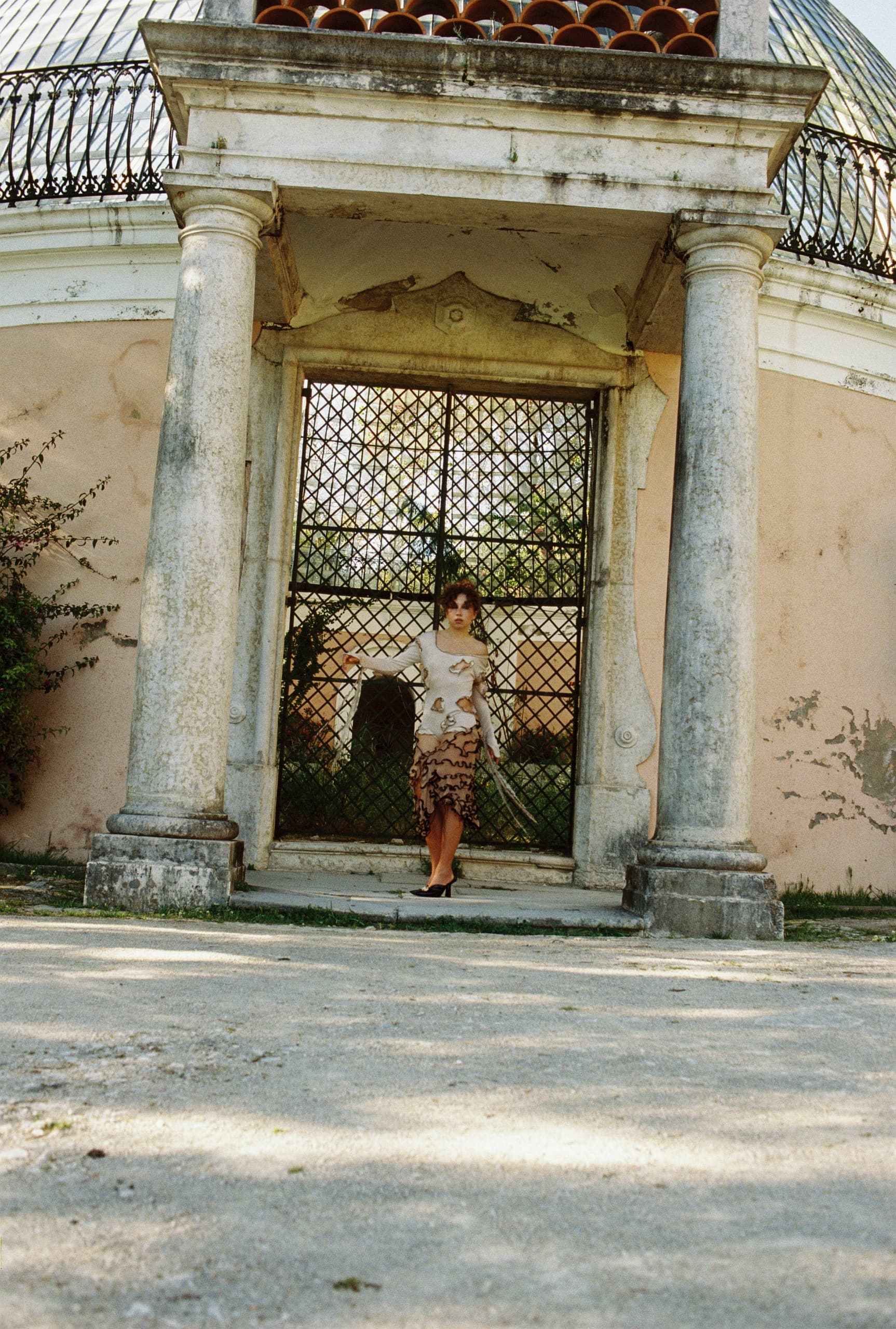 Woman in elegant dress standing by ornate building with columns.