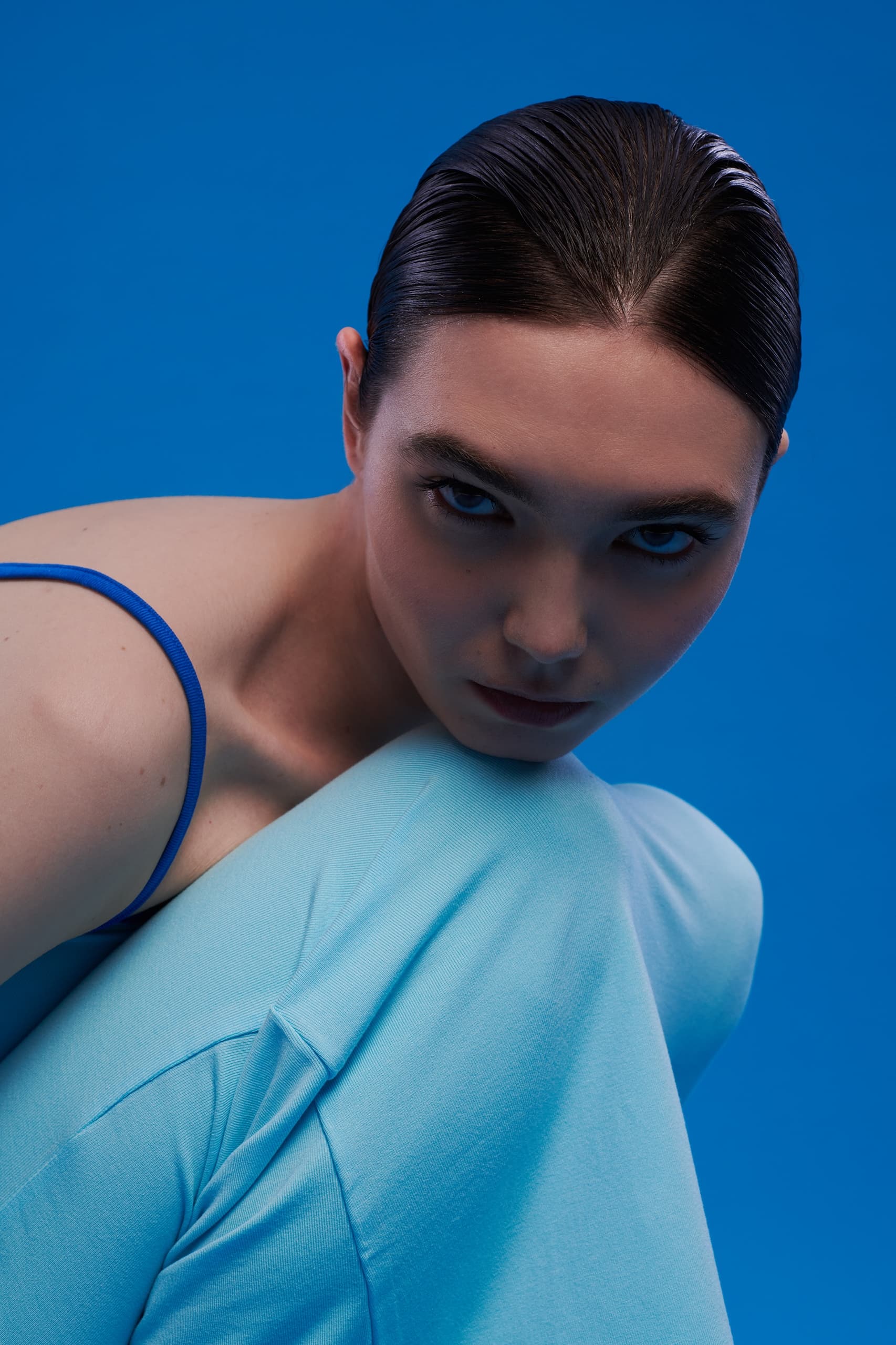 Model in blue outfit against blue background, intense gaze, fashion photography.