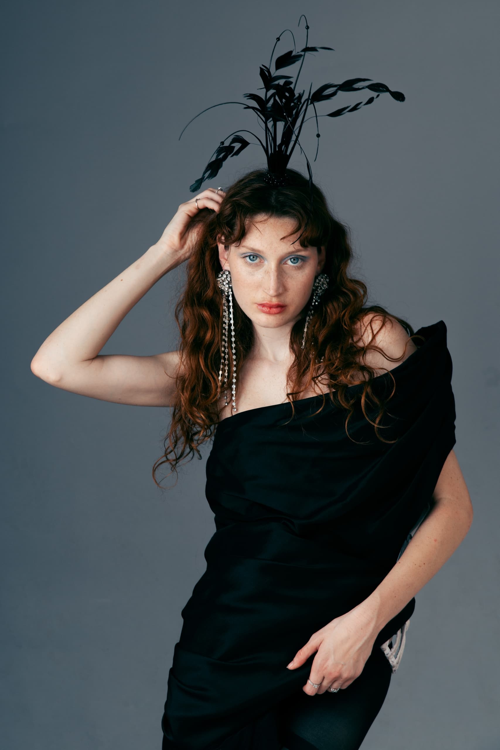 Woman in elegant black dress with artistic headpiece posing confidently.