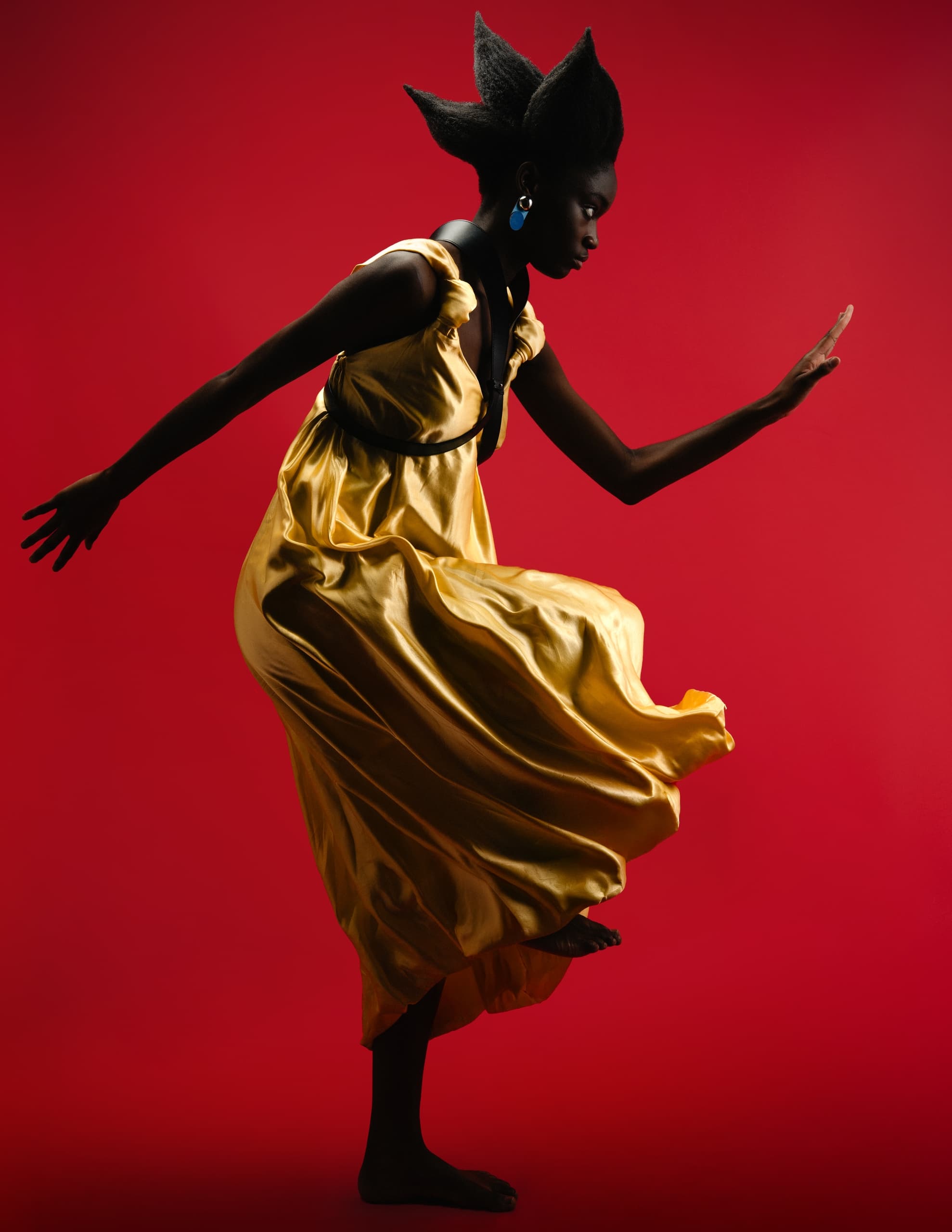 Dancer in flowing gold dress with bold hair against a red background.