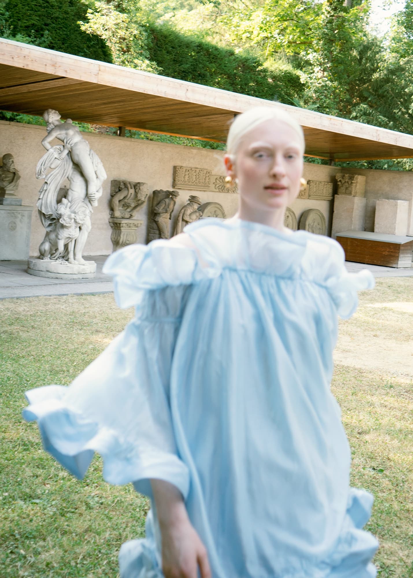 Person in blue dress by outdoor sculpture garden, blurred motion effect.