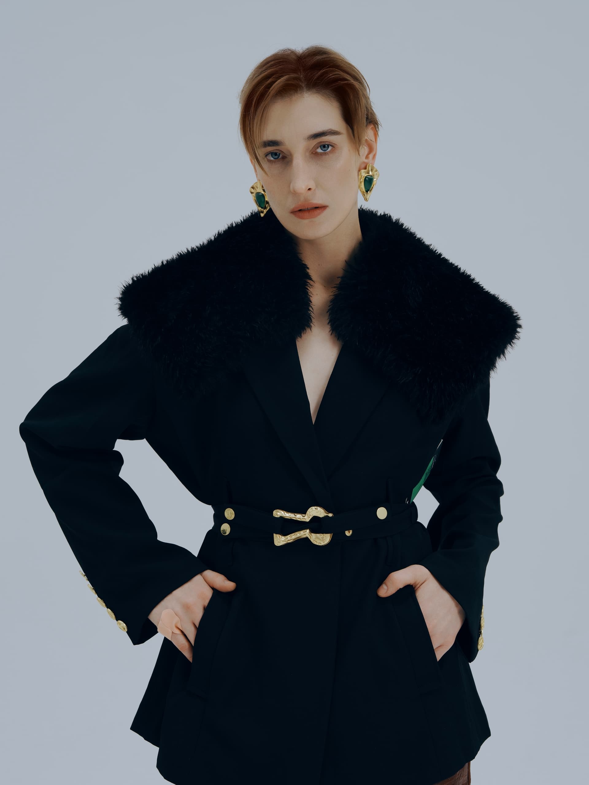 Fashionable person in a stylish black coat with a fur collar and bold earrings.