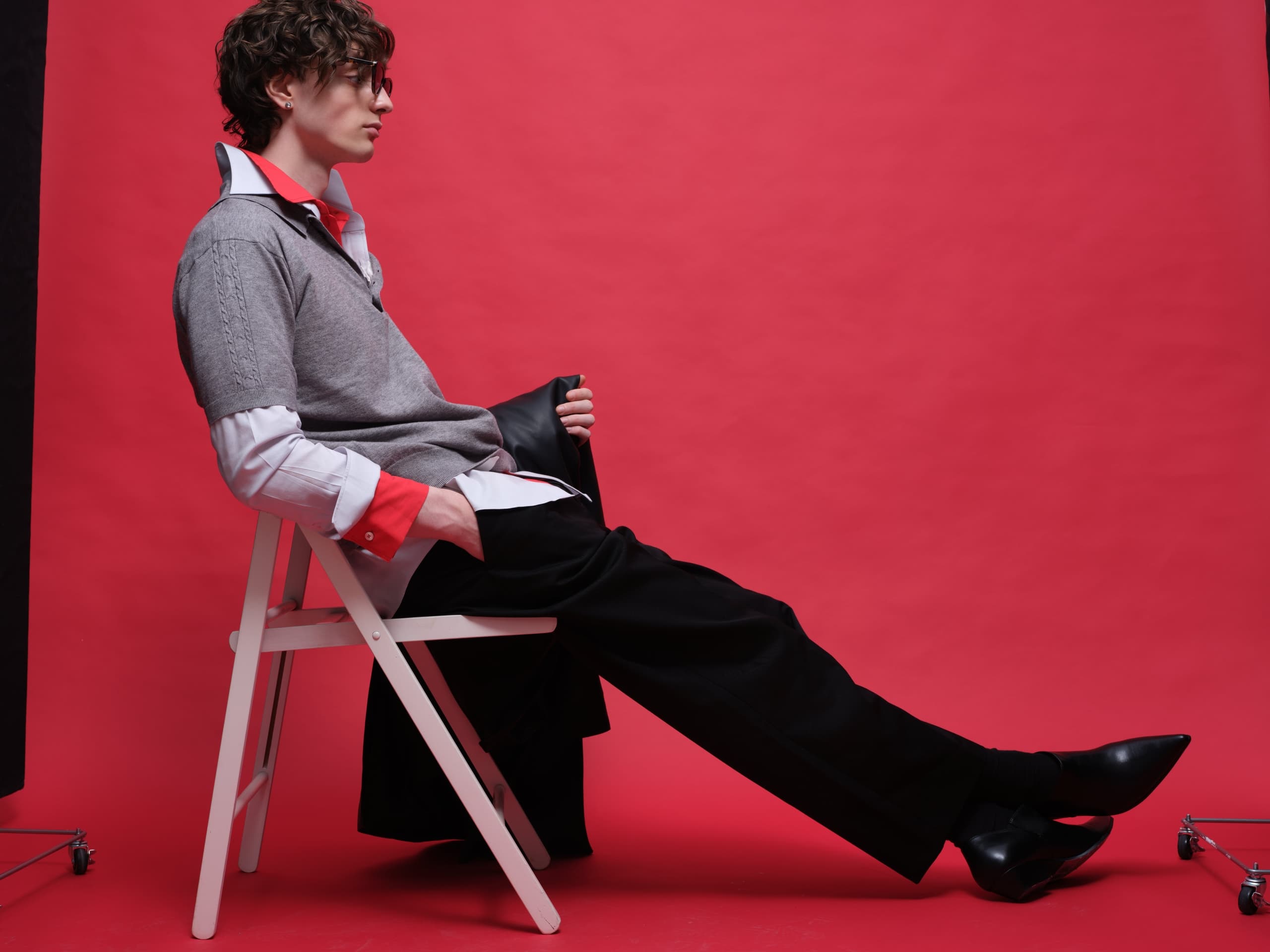 Stylish person seated on white chair against vibrant red backdrop.