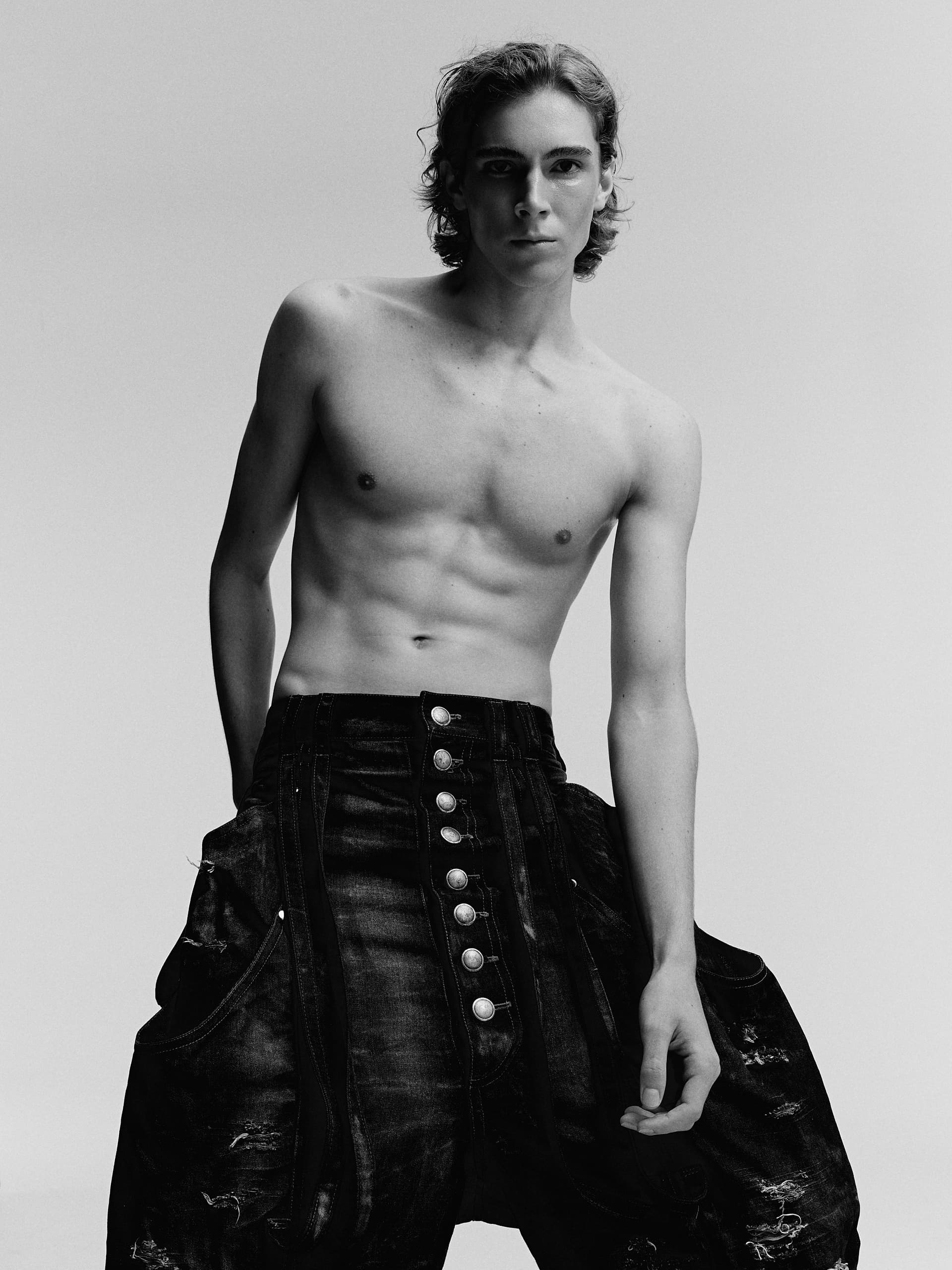 Shirtless model in stylish wide-leg jeans, striking a confident pose in a studio.