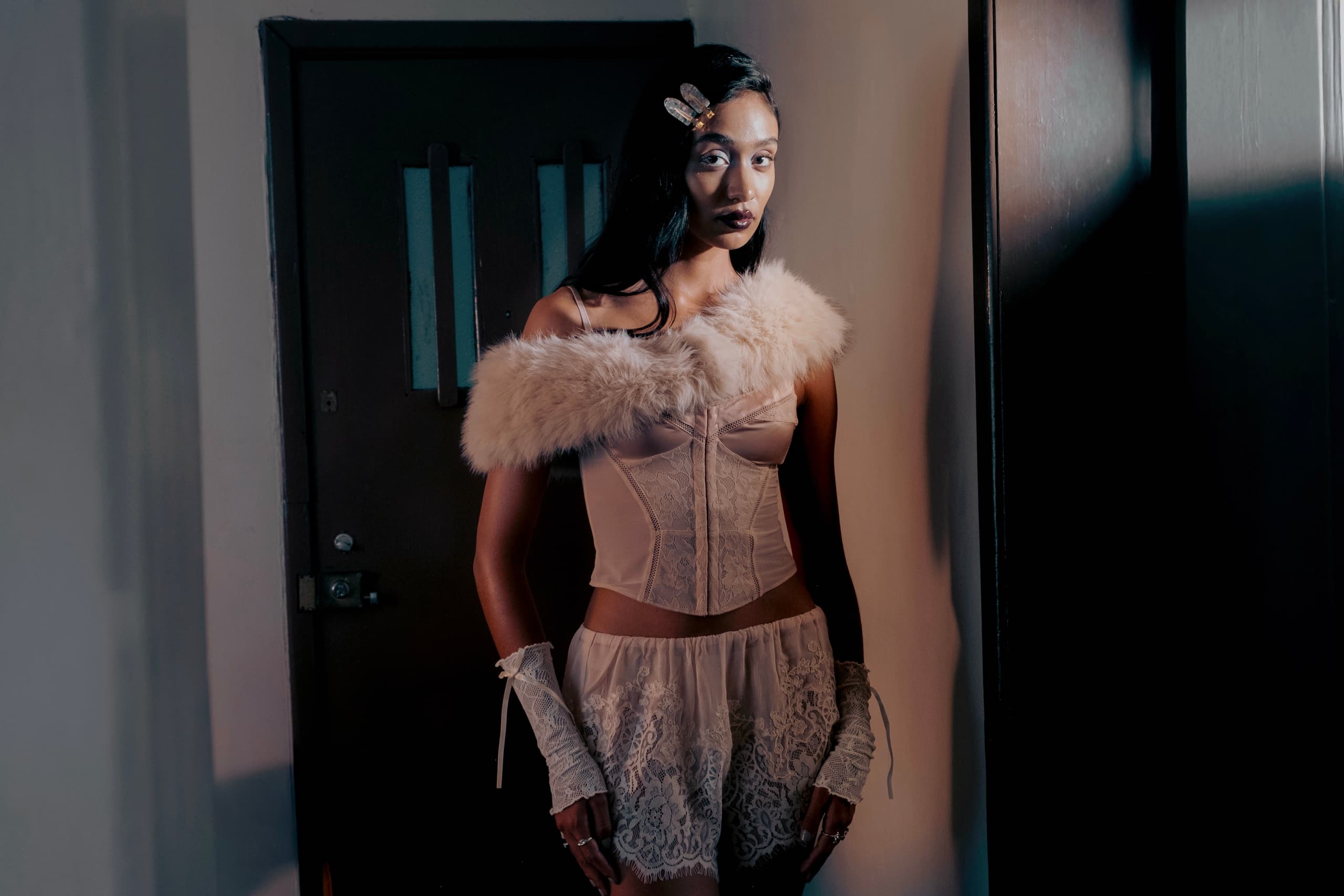 Fashionable woman in elegant lace attire and fur, standing indoors.