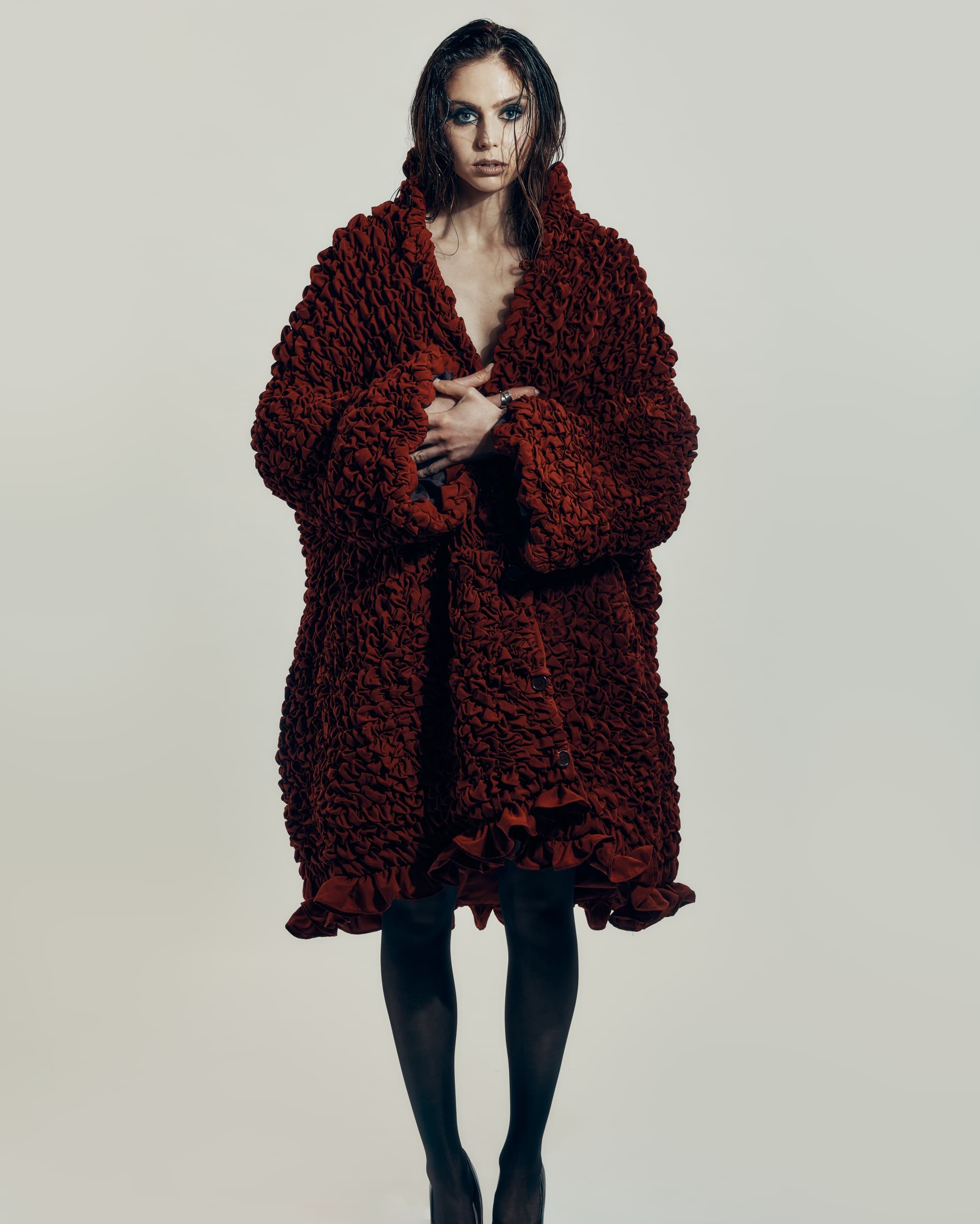 Model in textured red coat, bold makeup, striking fashion photography.