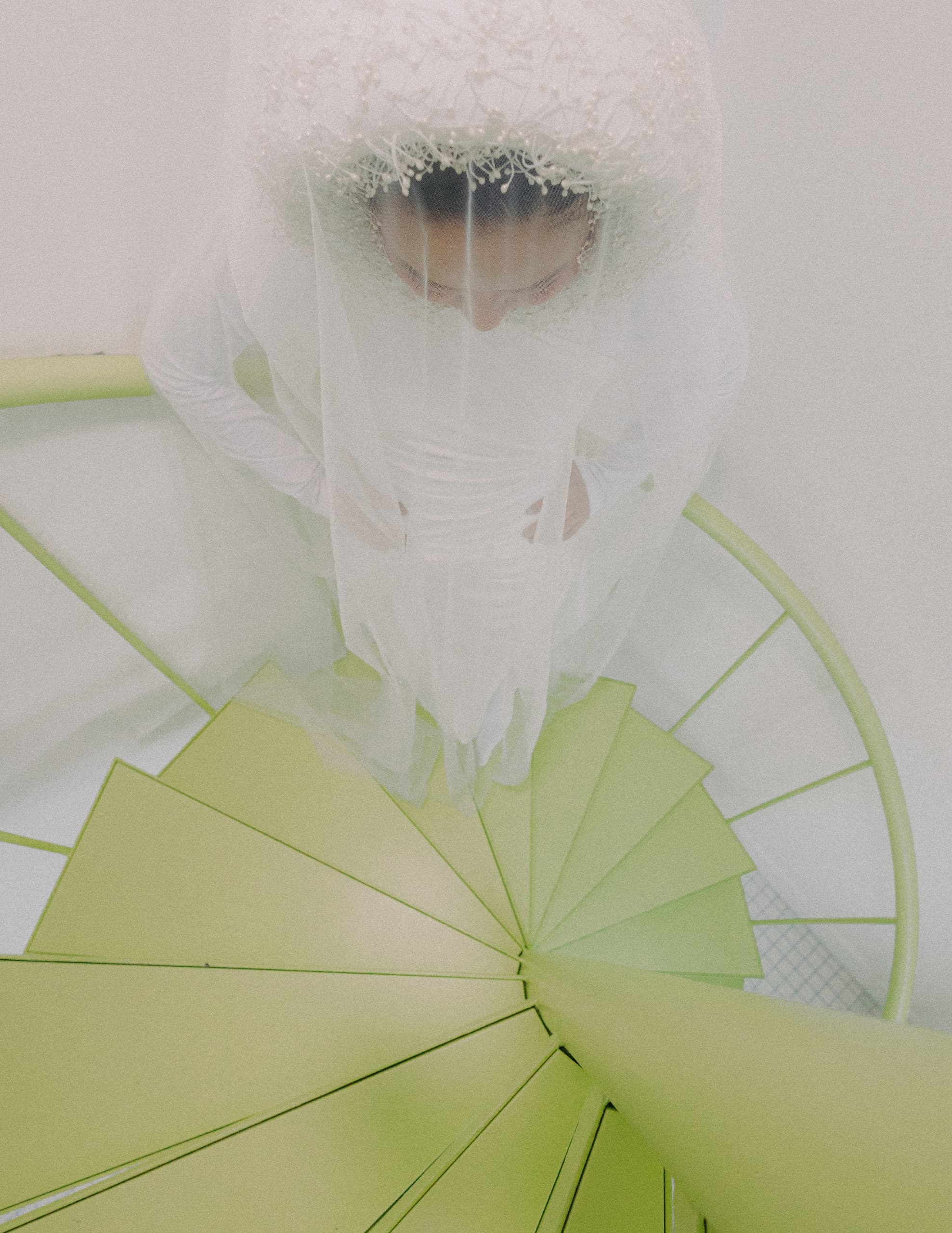 Bride in a white gown descending a green spiral staircase from above.
