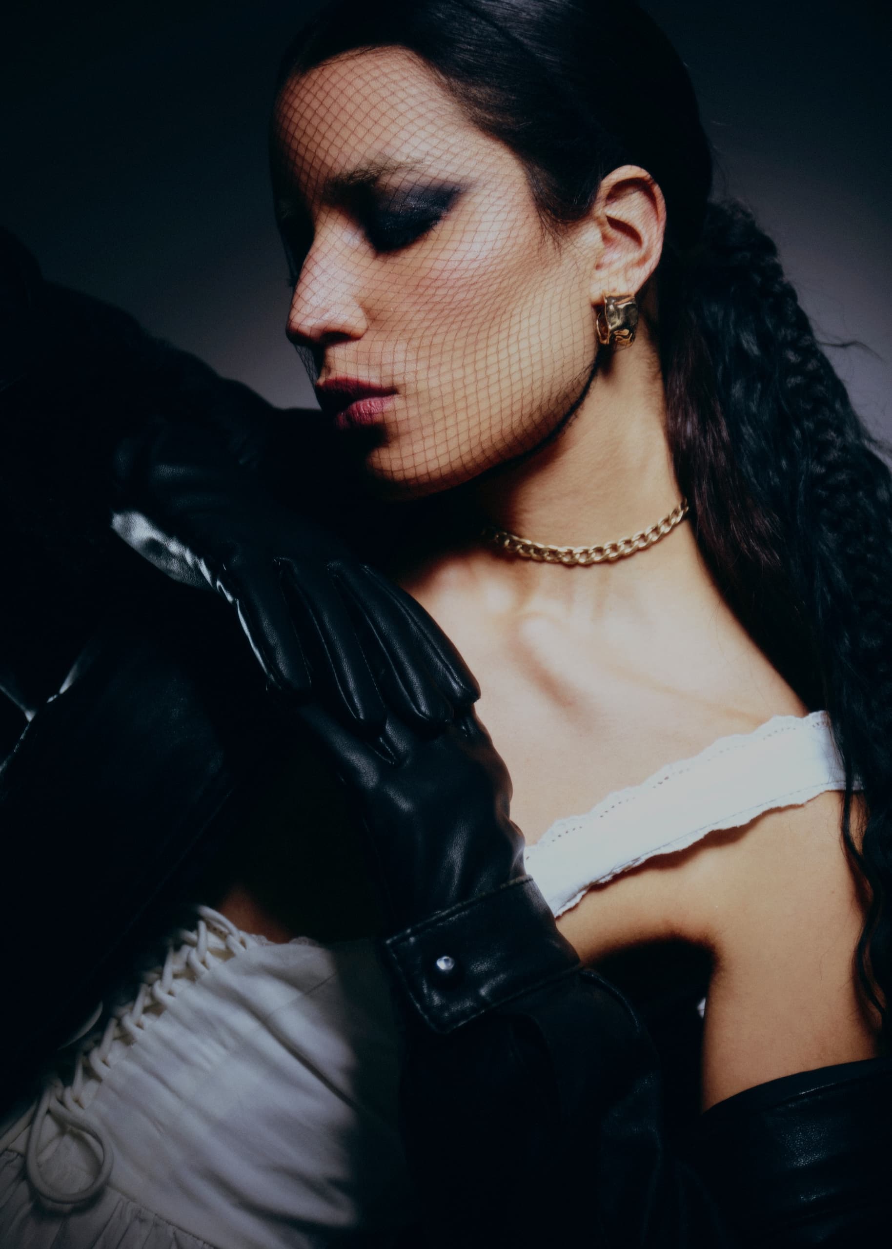 Elegant woman in black gloves, fishnet veil, gold jewelry, and white dress.